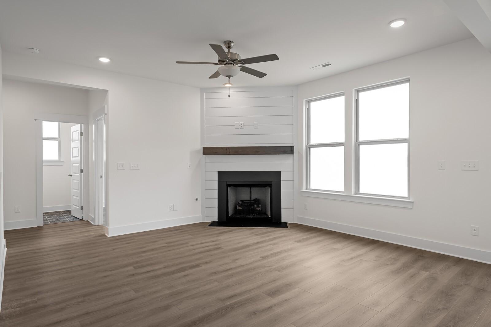 Spacious living room with shiplap gas fireplace, hardwood floors, ceiling fan, and large windows in Davidson Homes The Willow C, Gallatin, TN