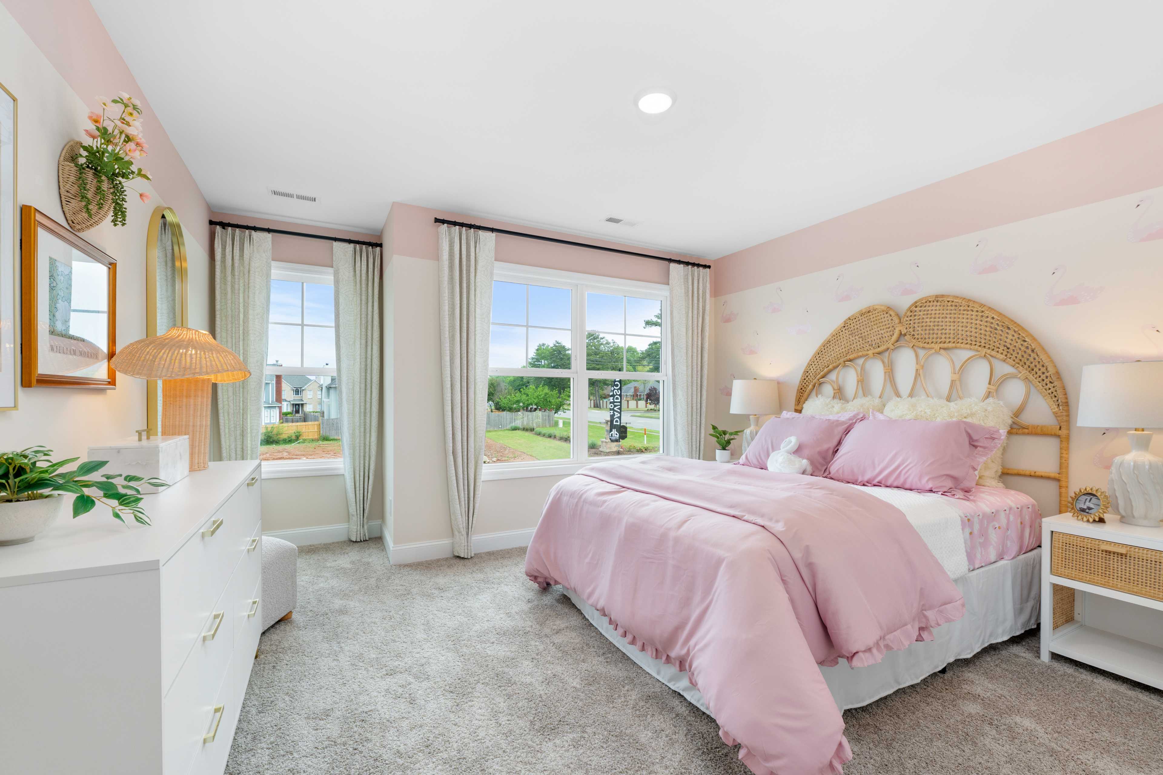 Charming pink bedroom at Pavilion in Huntsville AL by Davidson Homes with rattan headboard, white dresser, plants, and garden window view