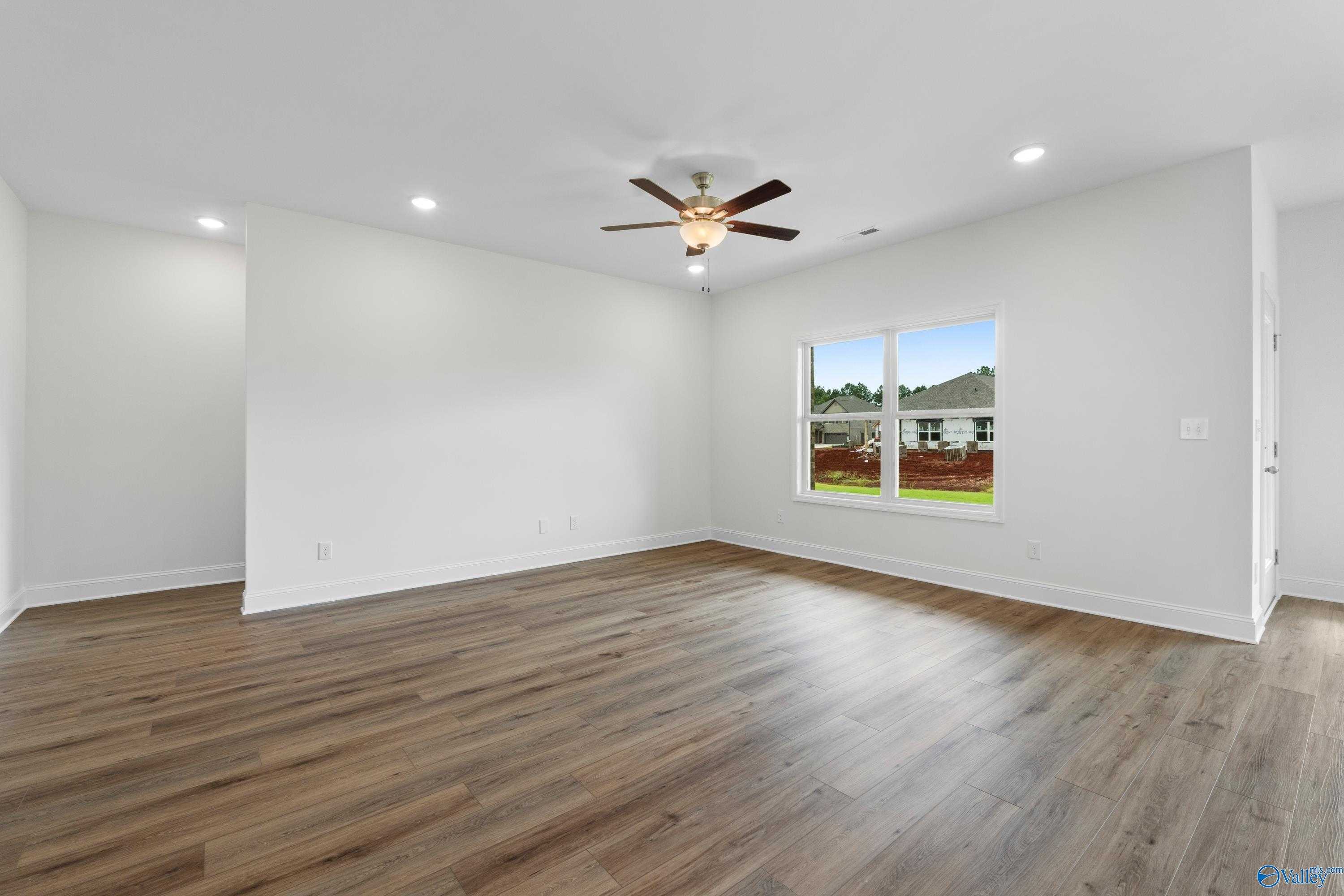 Bright empty living room with hardwood floors, ceiling fan, and large window overlooking backyard in Davidson Homes The Asheville C, Athens, Alabama