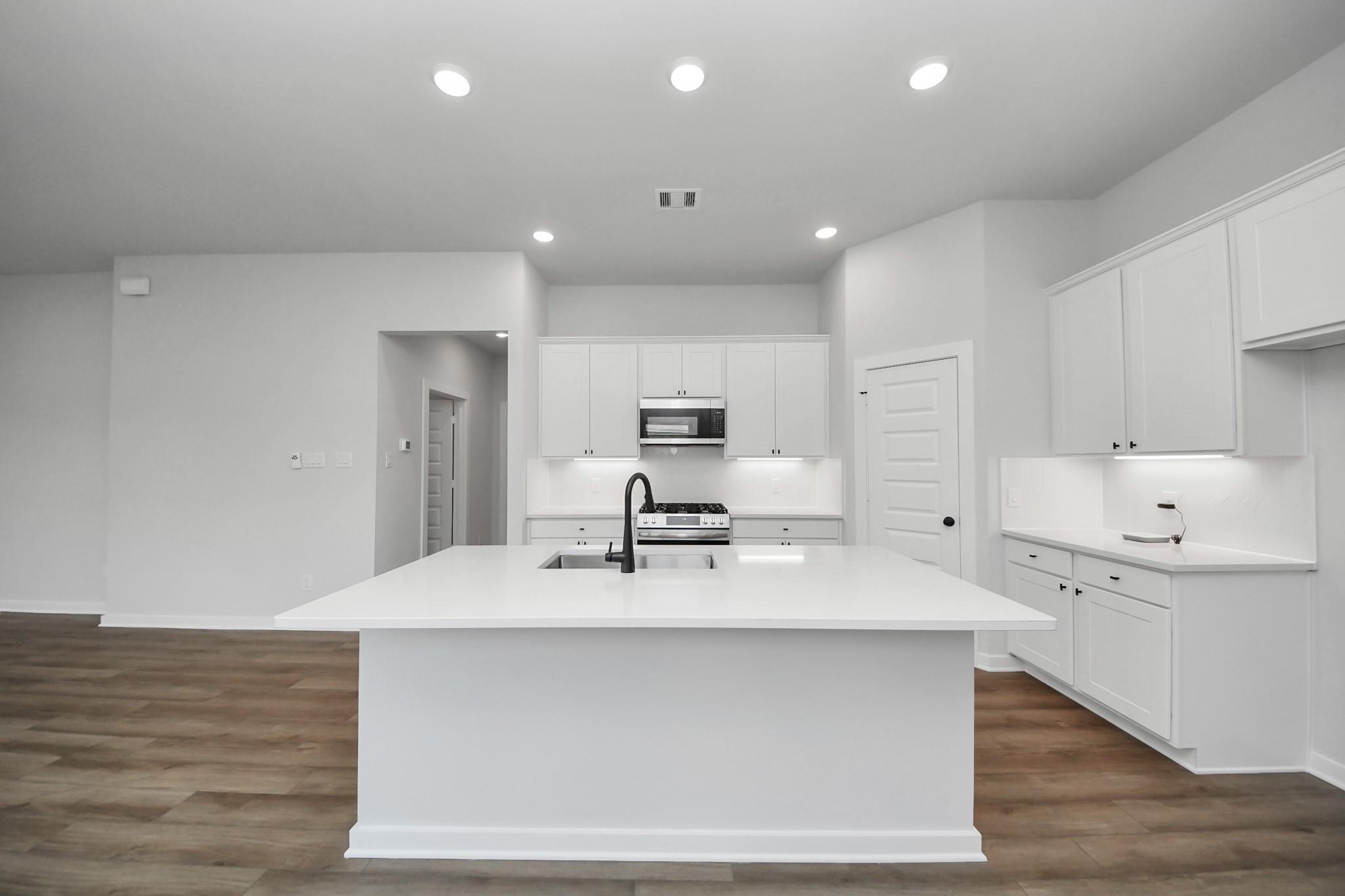 Modern white kitchen with large island and stainless appliances in The Riviera C home at River Ranch Meadows, Dayton, Texas.