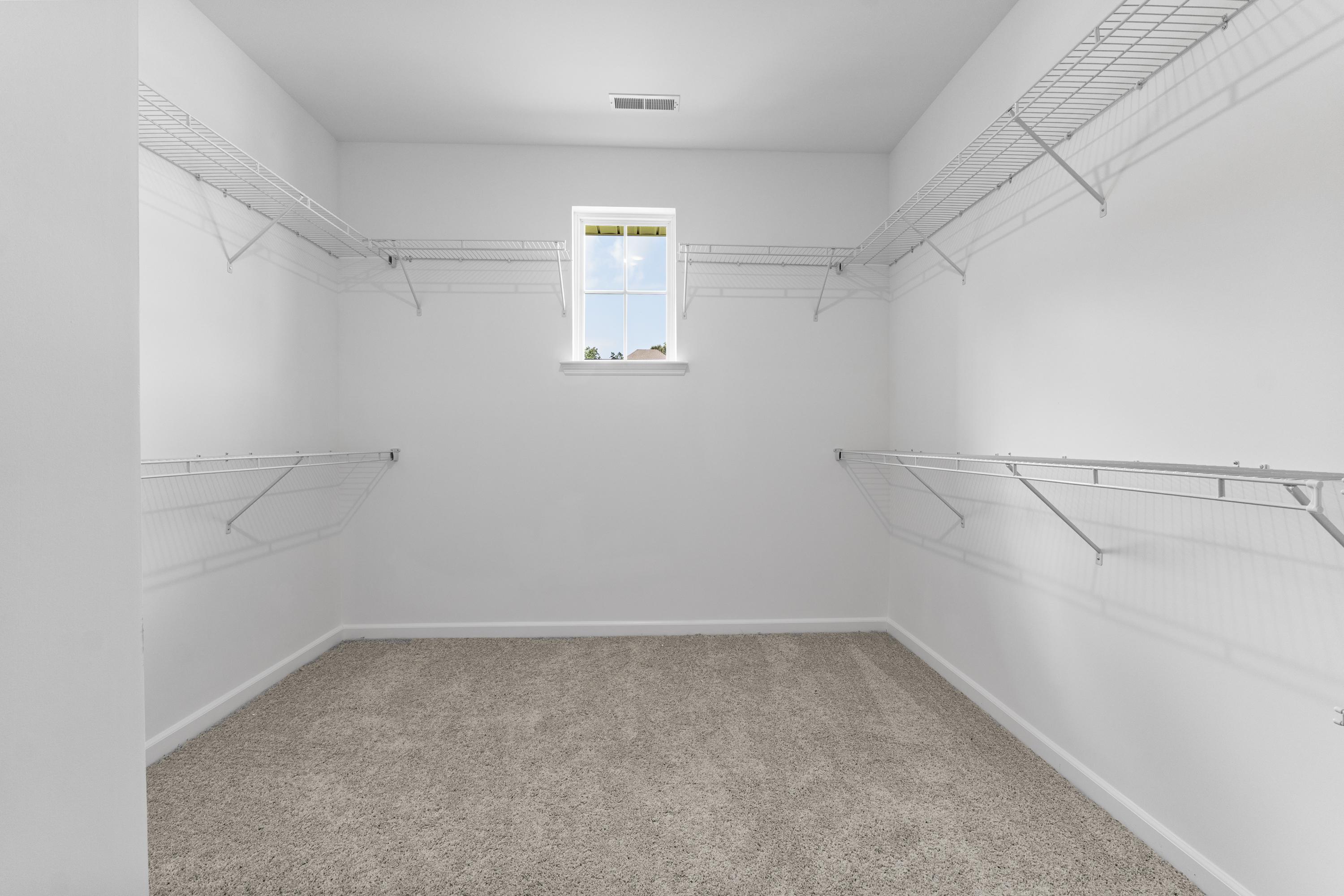 Spacious walk-in closet in The Avalon D master suite with wire shelving, natural light window, and beige carpet floor