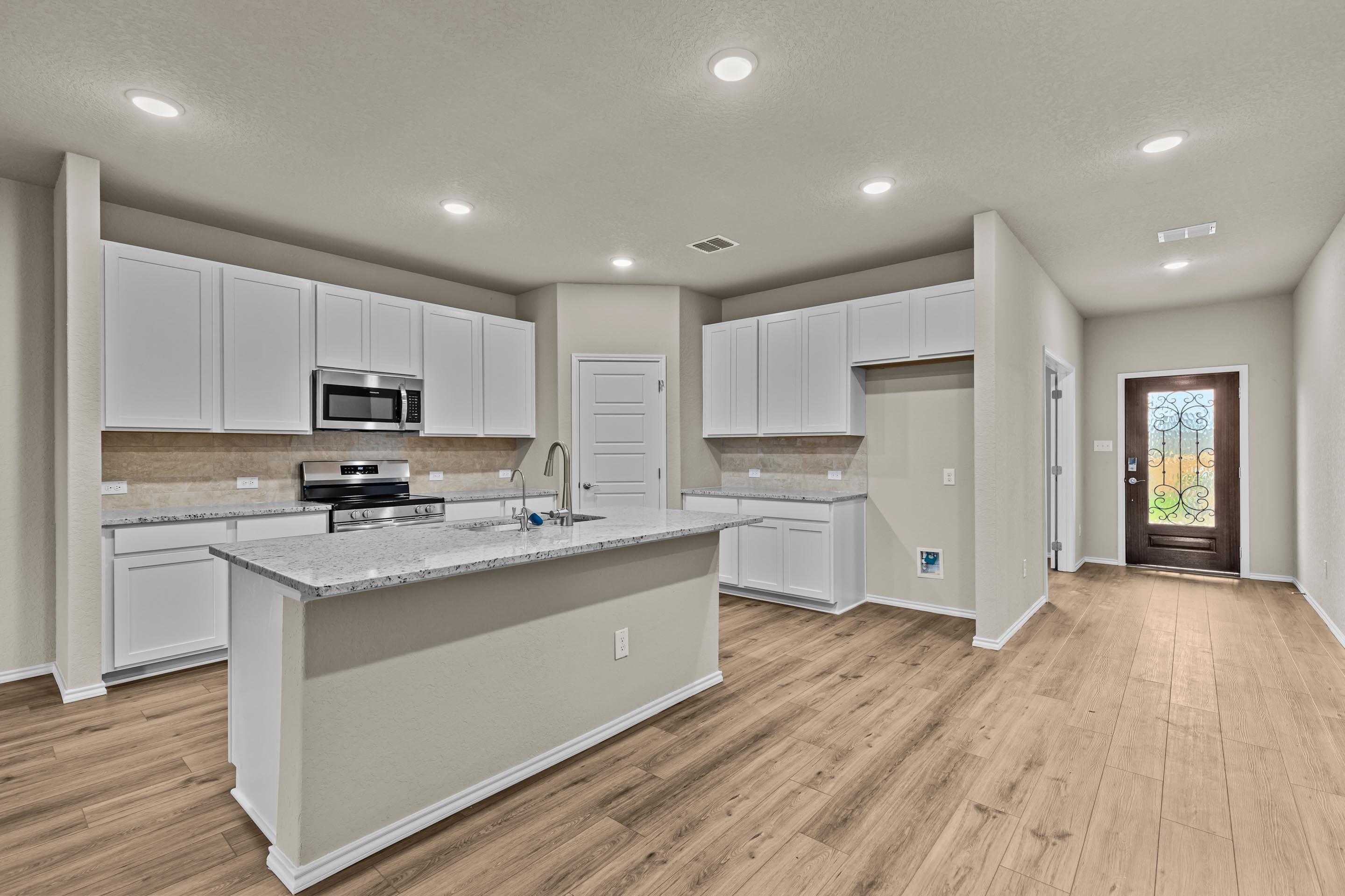 Modern open-concept kitchen with white cabinets, granite island, stainless appliances, and hardwood floors in Davidson Homes The Douglas F, San Antonio