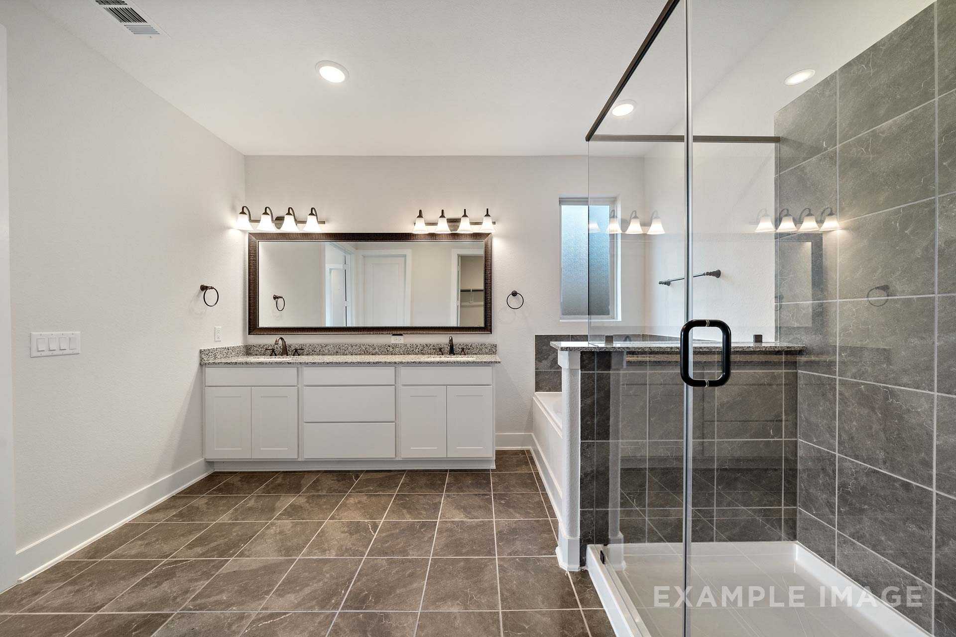 Luxurious master bathroom in The Victoria A featuring double vanity, frameless glass shower, and modern tile flooring