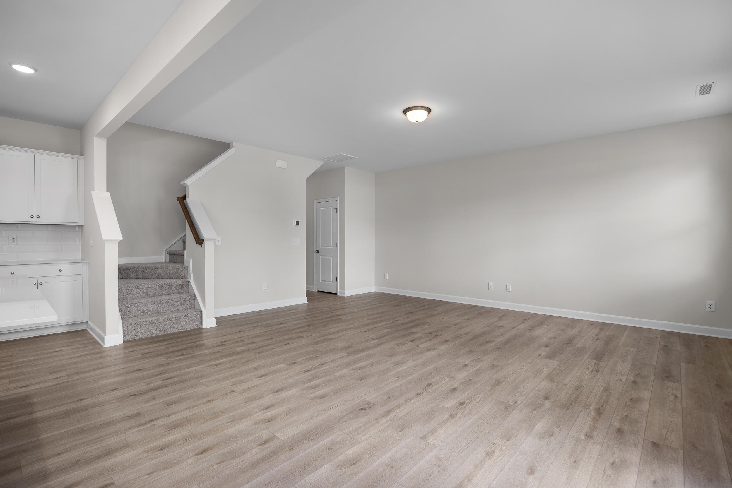 Spacious open-concept kitchen and living area in The Grace A with white cabinets, hardwood floors, and carpeted staircase