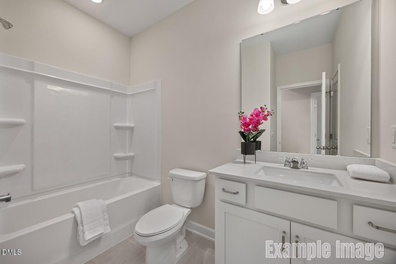 Bright bathroom with white tub-shower combo, vanity, and toilet in The Carter C 3-bedroom home, Lillington, North Carolina