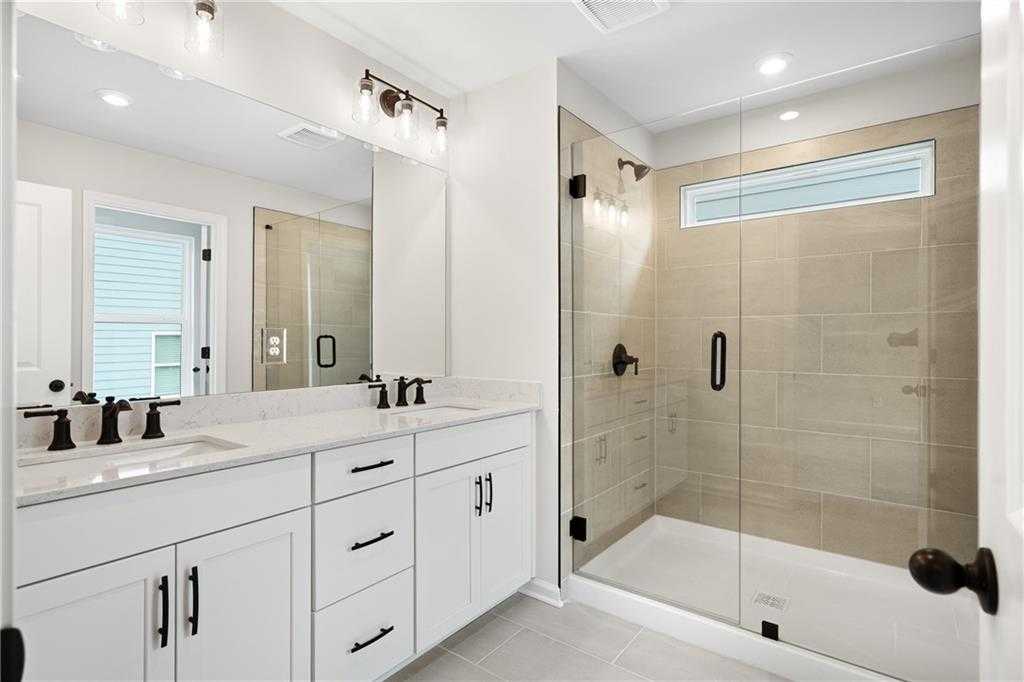 Modern master bathroom featuring double vanity, frameless glass shower, and neutral tile in Davidson Homes The Marion A, Kennesaw, Georgia