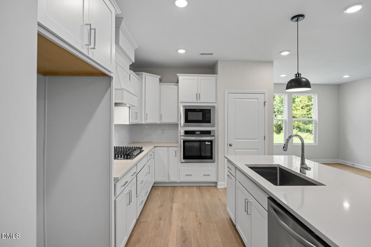 Modern kitchen with white shaker cabinets, quartz island, and stainless appliances in The Daphne D plan, Woodland Crossing, Zebulon NC