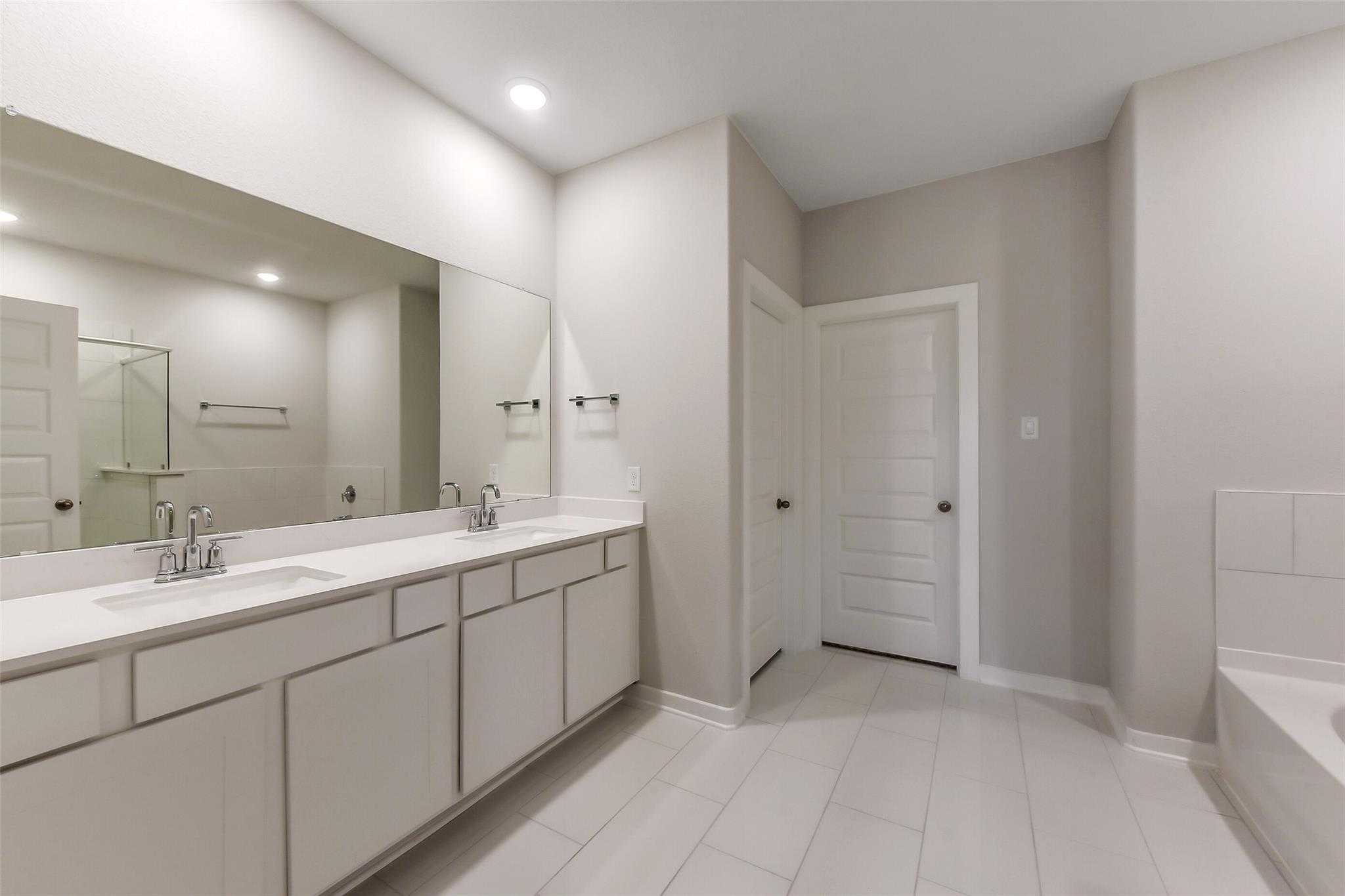 Elegant master bathroom with double vanity, large mirrors, white cabinets, and soaking tub in Davidson Homes The Laguna B, Katy, Texas