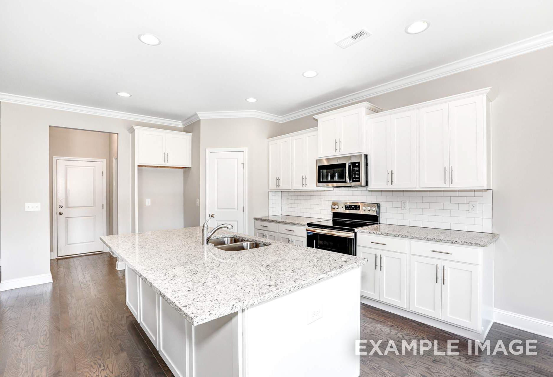 Spacious white kitchen in The Montgomery B featuring granite island, shaker cabinets, subway tile backsplash, and stainless steel appliances