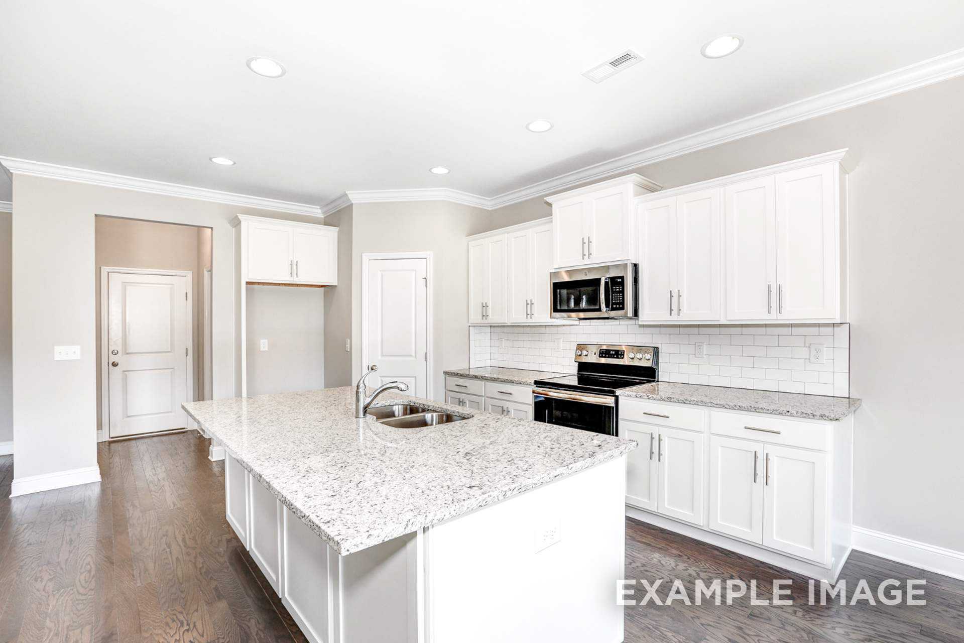 Spacious kitchen in The Montgomery C with white shaker cabinets, granite island, subway tile backsplash, and hardwood floors