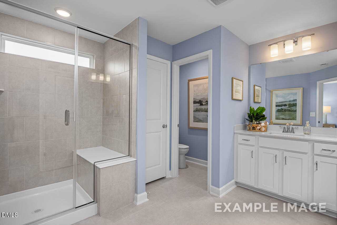Modern master bathroom with frameless glass shower, double vanity, blue walls, and coastal art in Davidson Homes The Graham, Fuquay-Varina, NC