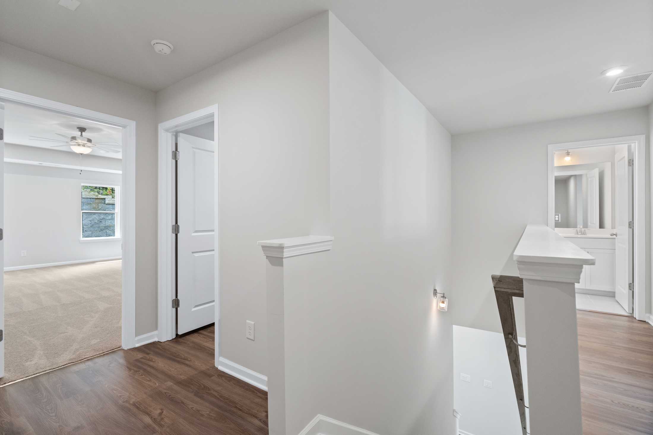 Upper floor hallway in The Cary A 2-story home by Davidson Homes, Winder GA, with white walls, wood floors, and staircase railing