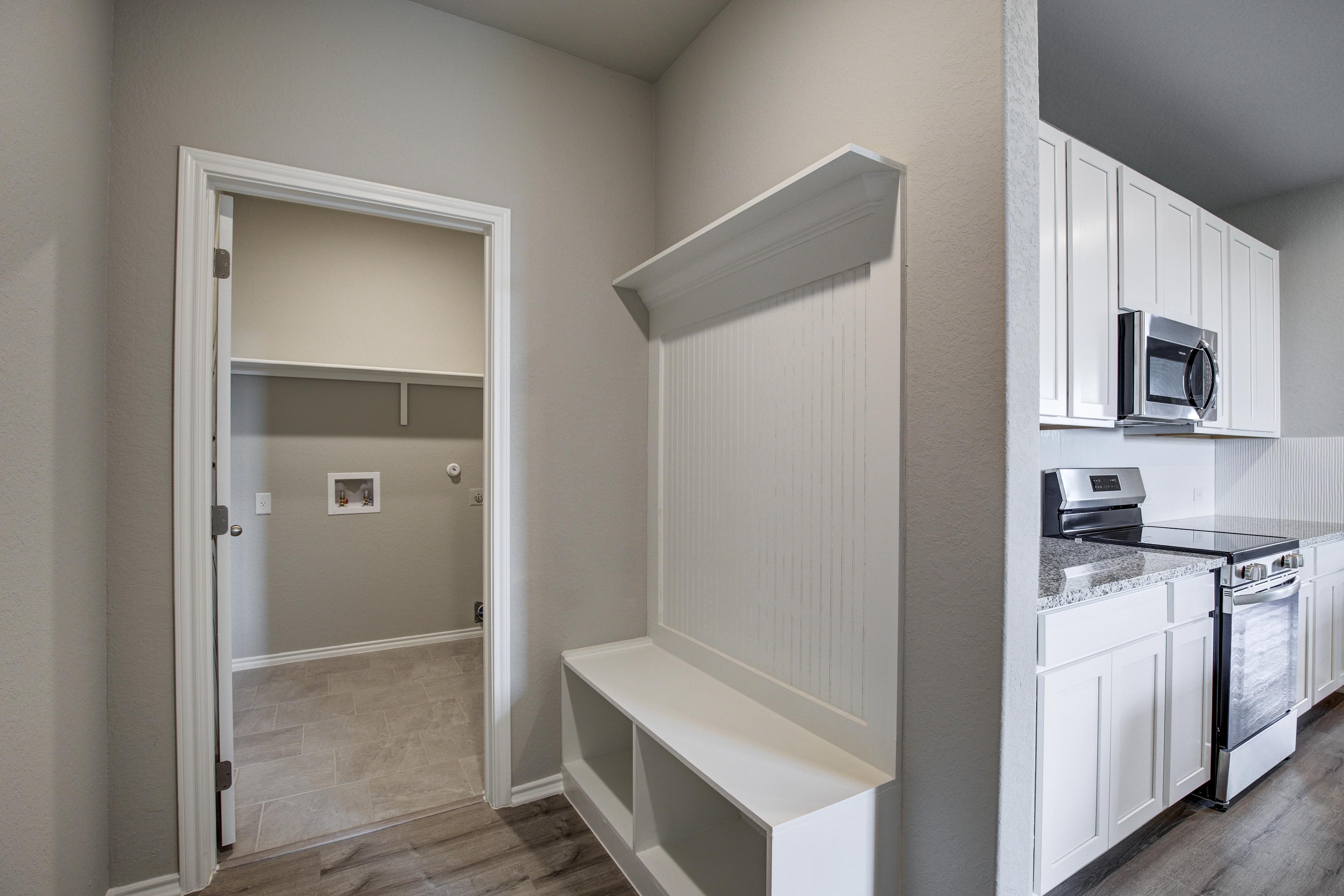 Laundry and mudroom in The Blanco C by Davidson Homes, with built-in white bench, hooks, washer-dryer nook, and adjacent kitchen appliances
