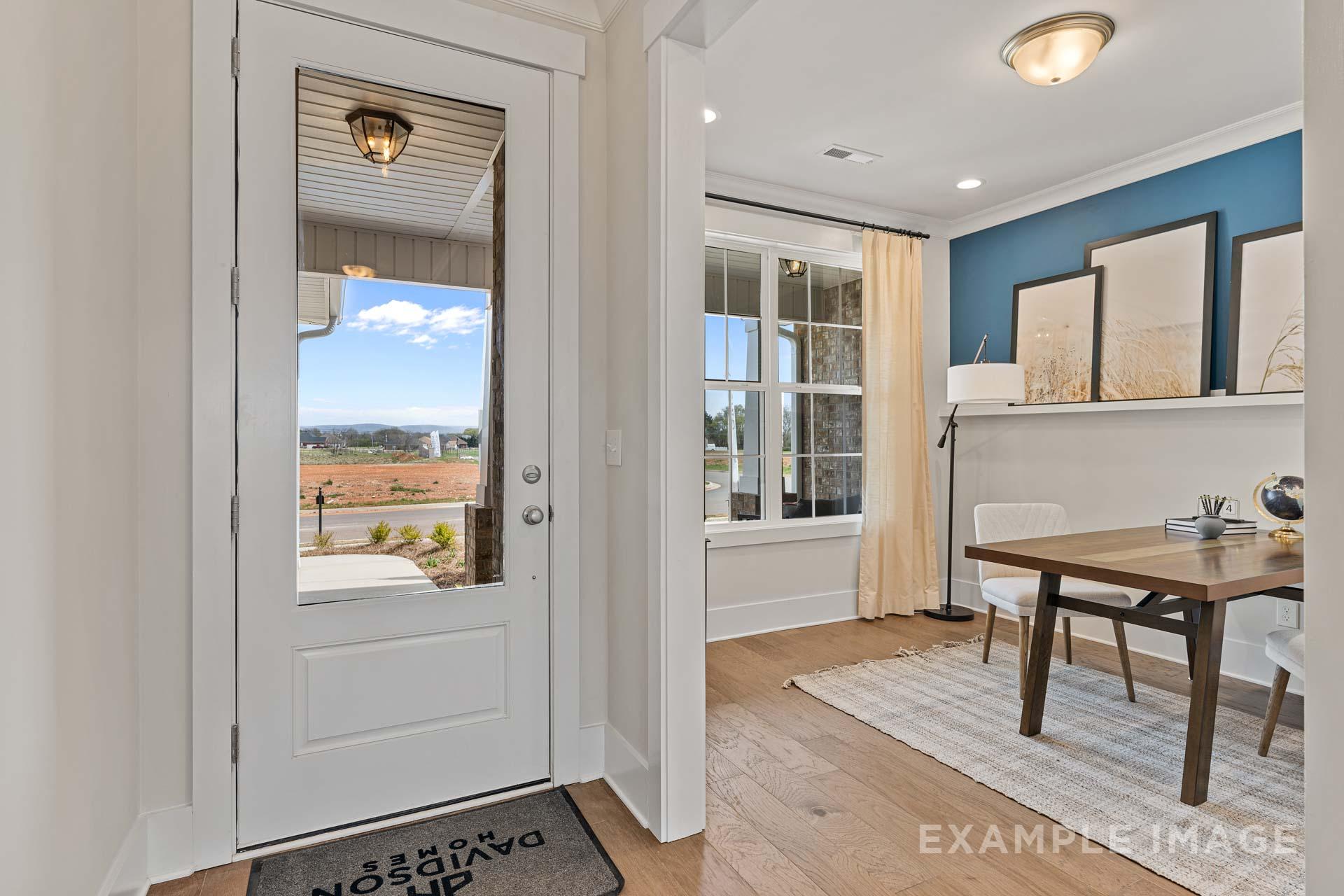 The Rockford home entryway by Davidson Homes: Open white door with scenic outdoor view, adjacent blue study featuring desk, lamp, artwork, and hardwood floors