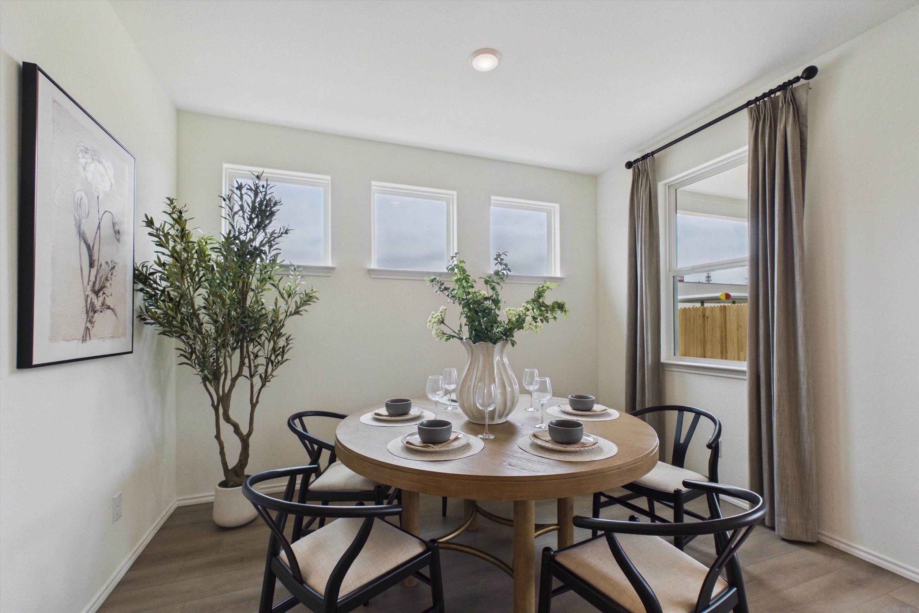Elegant dining room in Rayburn Valley San Antonio TX featuring round oak table, black chairs, floral vase centerpiece, potted olive tree, and large windows