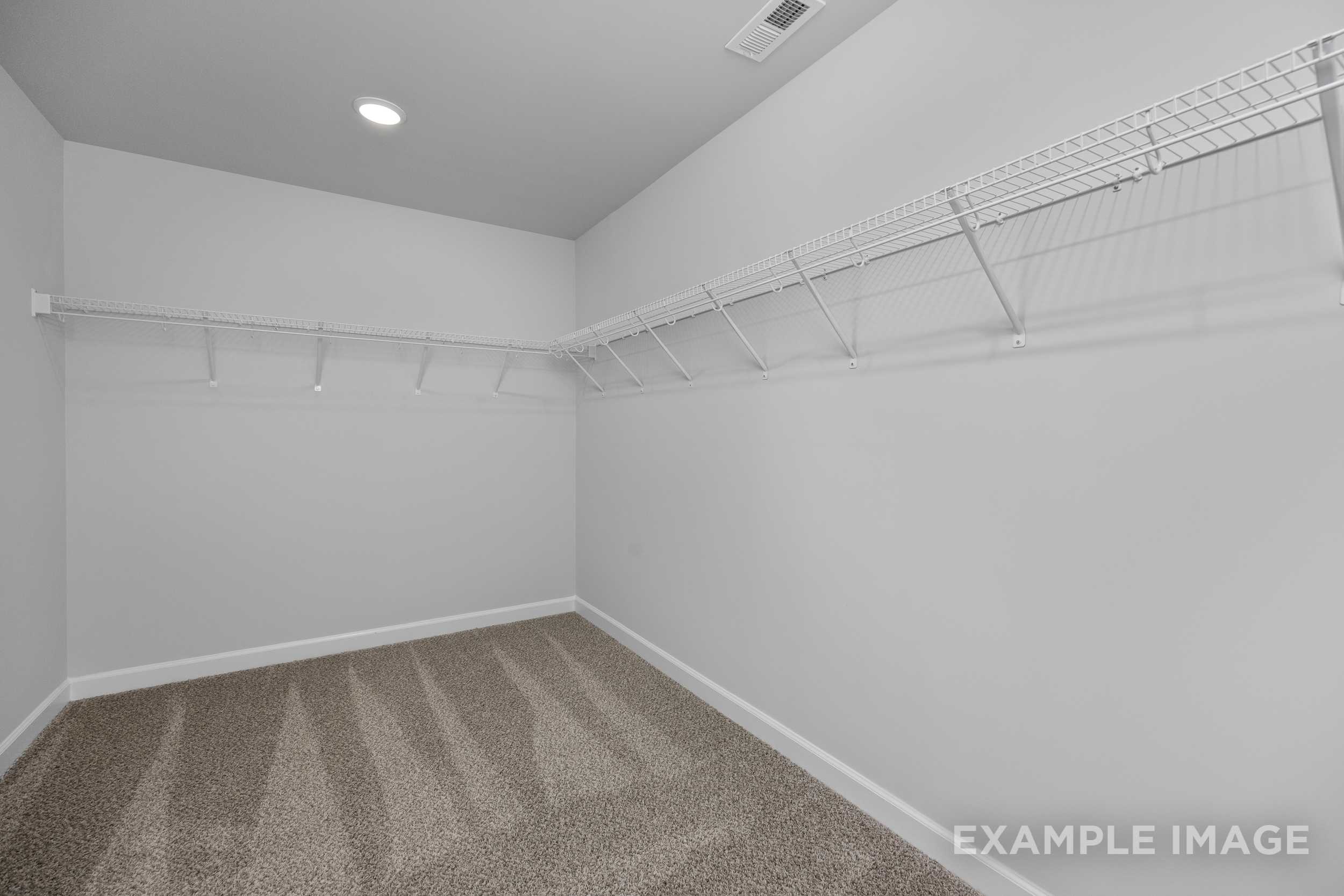 Spacious walk-in closet in The Hickory II master suite featuring wire shelving, beige carpet flooring, and recessed lighting