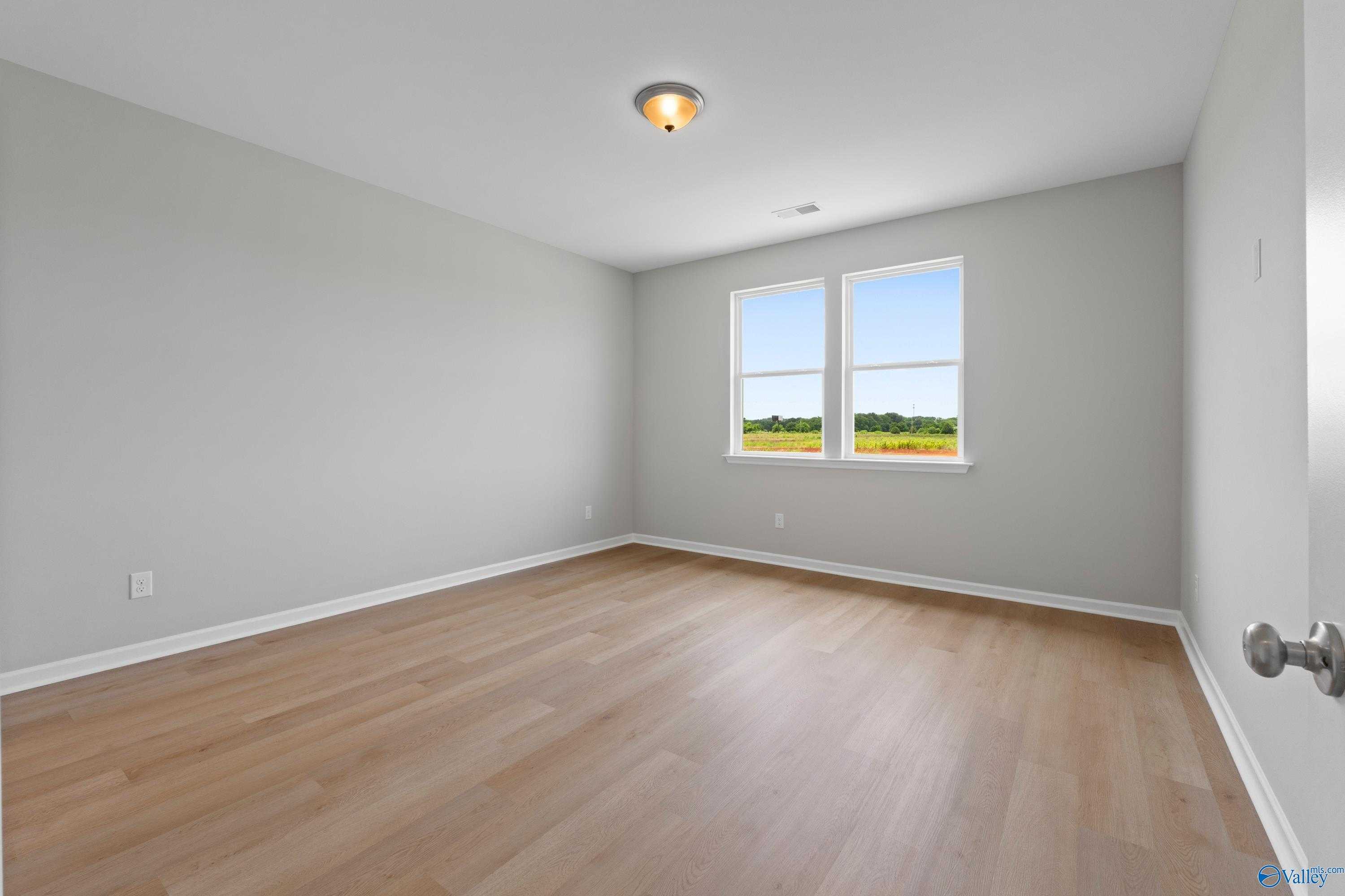 Bright secondary bedroom with gray walls, hardwood floors, and window views in Davidson Homes The Orion, Athens, Alabama