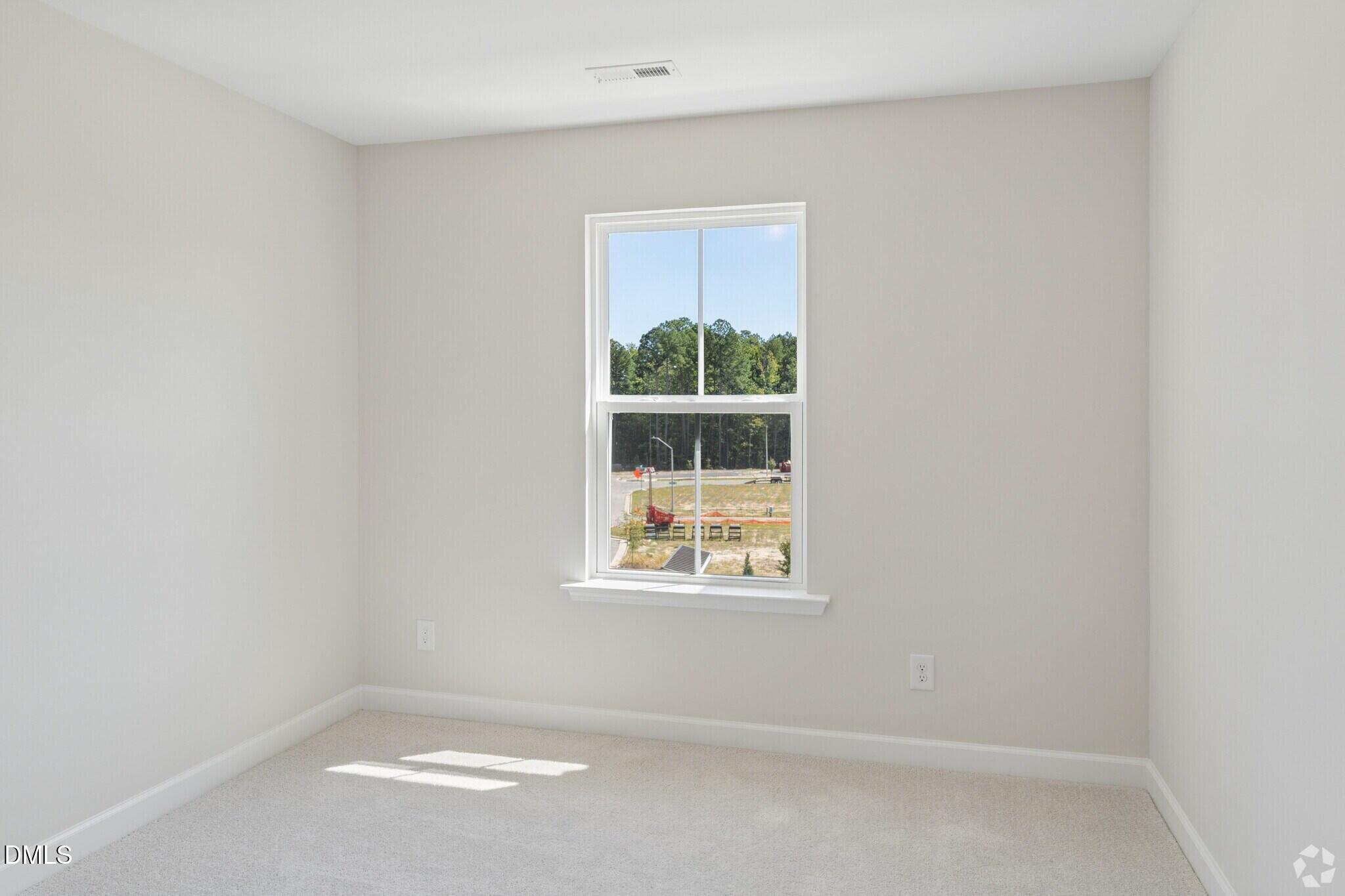 Bright empty bedroom with new carpet and white double-hung window in Davidson Homes The Avery townhome, Knightdale, NC