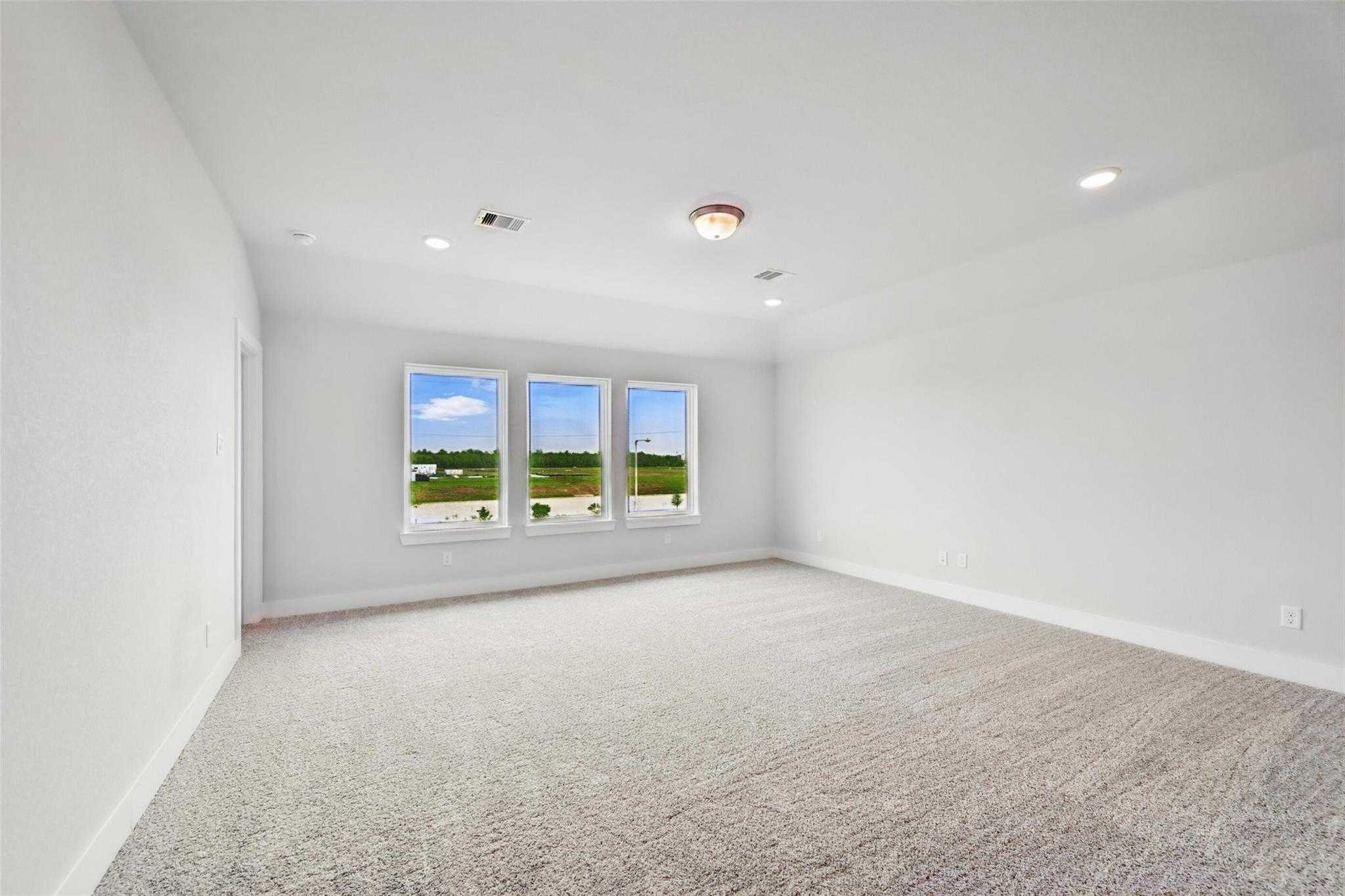 Bright upstairs bonus room with beige carpet, large triple windows overlooking green fields and sky in The Philip A, Lago Mar home