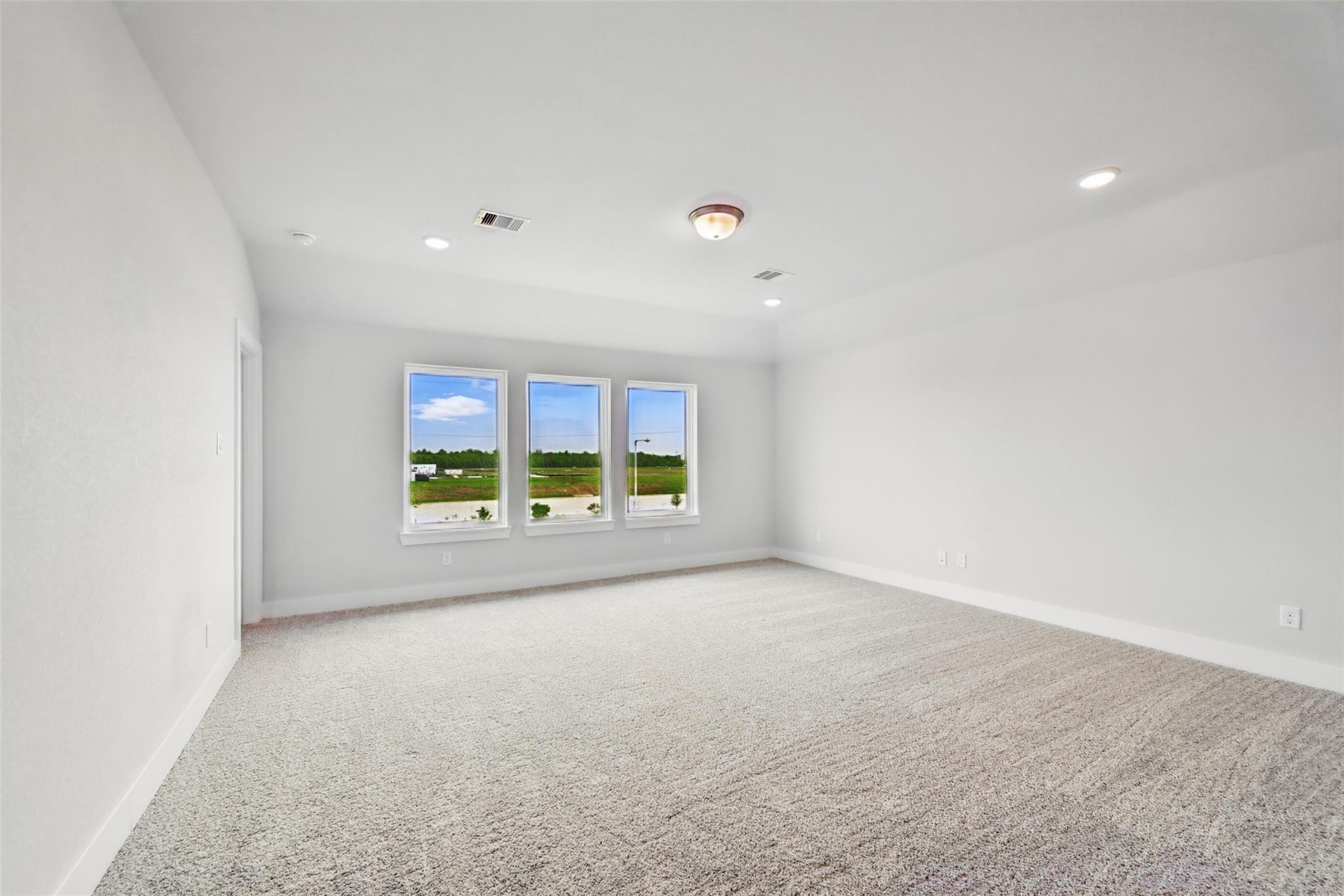 Bright upstairs bonus room with beige carpet, large triple windows overlooking green fields and sky in The Philip A, Lago Mar home