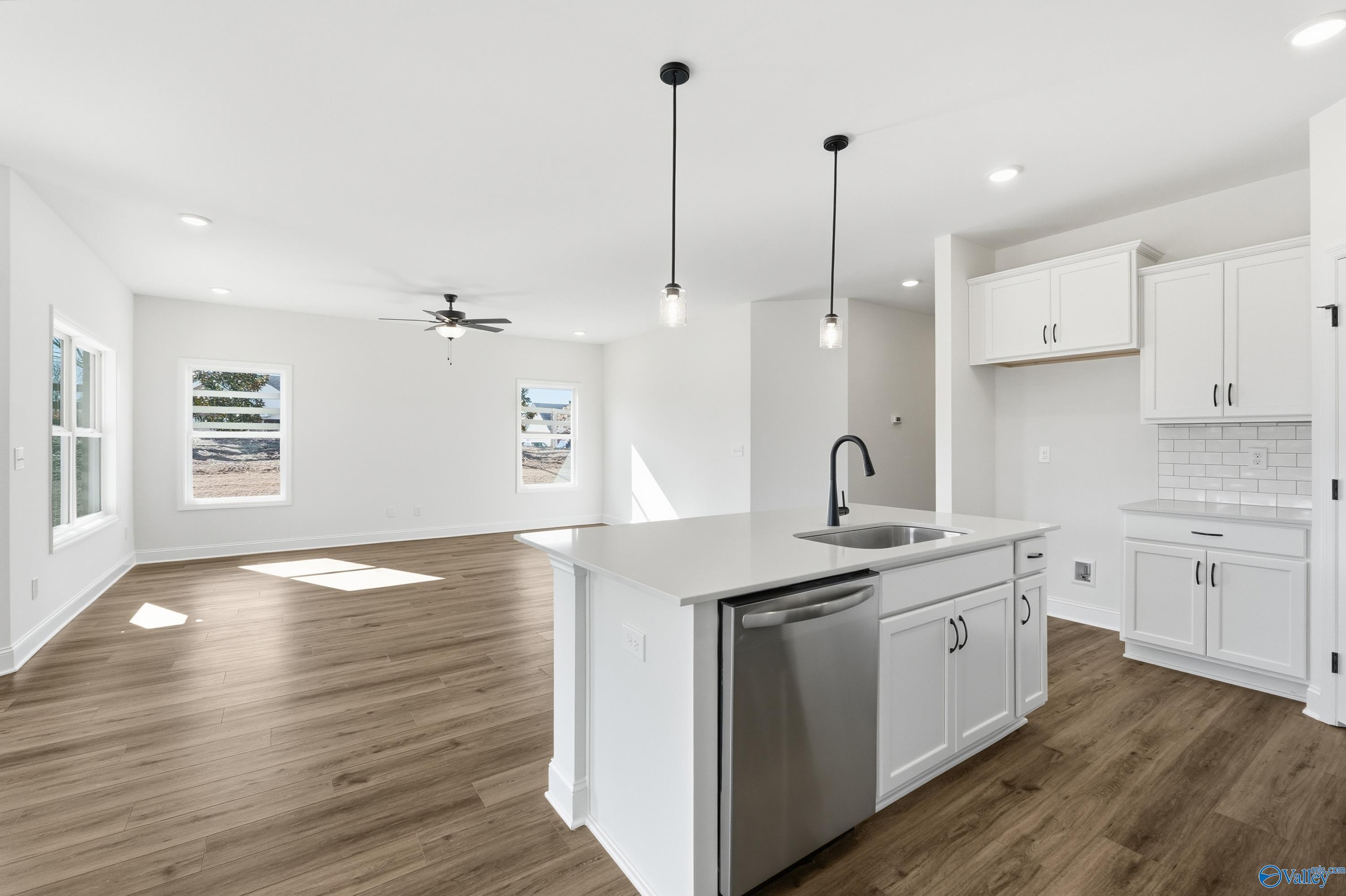 Modern open-concept kitchen with white cabinets, quartz island sink, stainless dishwasher, and LVP flooring in Davidson Homes The Franklin C, New Market, AL