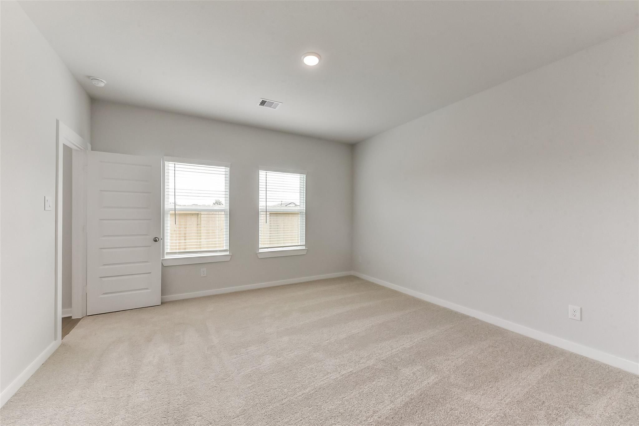 Spacious empty bedroom with light gray walls, beige carpet, and two window blinds in Davidson Homes The Sabine F, Dayton, Texas