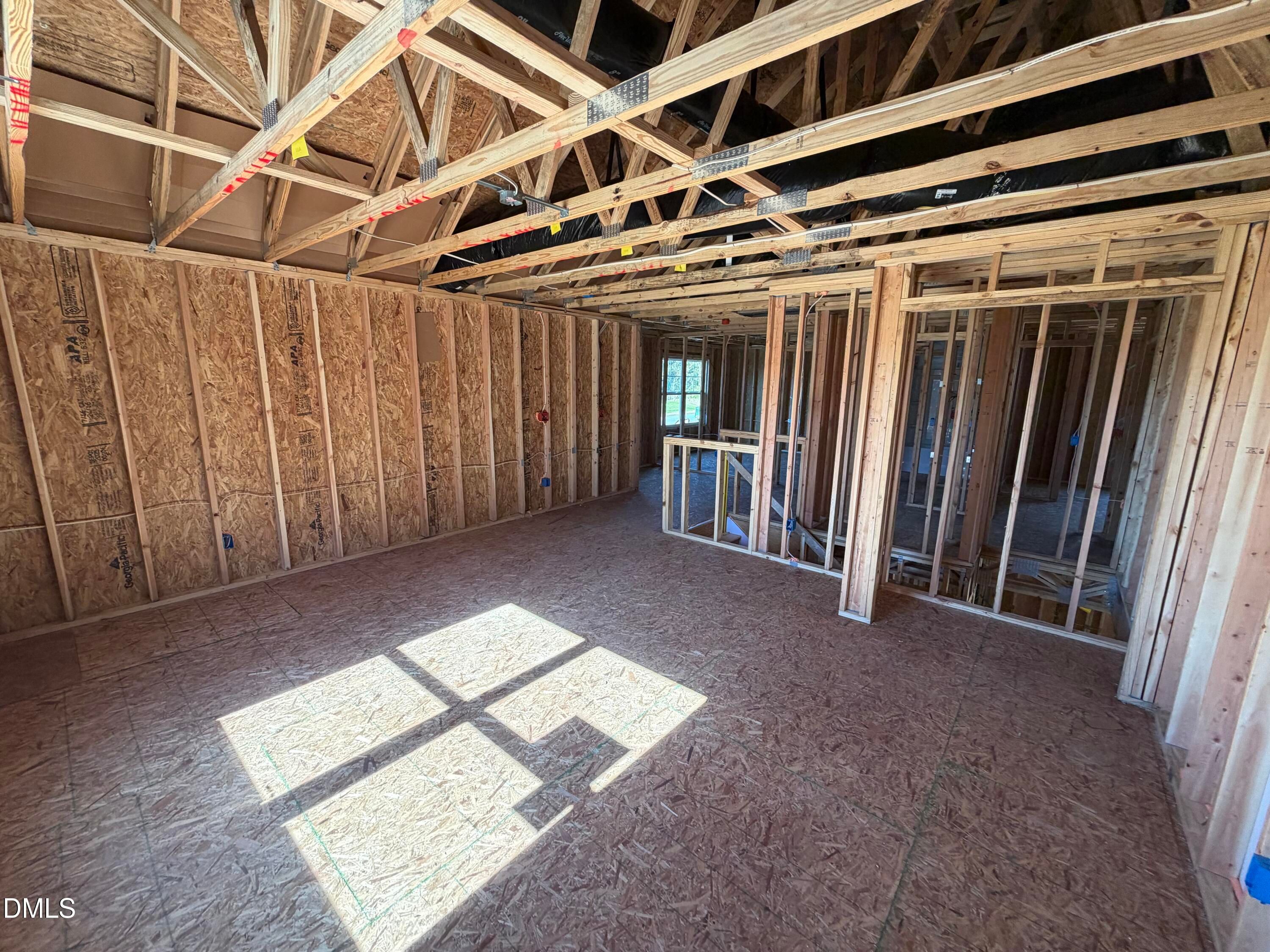Spacious open framing with wooden studs, ceiling joists, and sunlight in The Ash B 3-bedroom home by Davidson Homes, Lillington, NC
