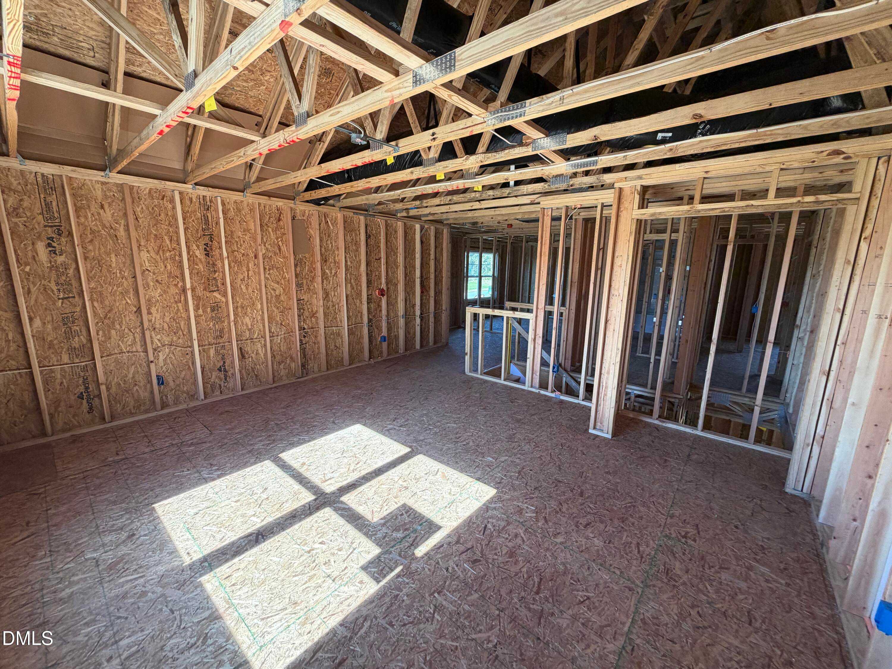 Spacious open framing with wooden studs, ceiling joists, and sunlight in The Ash B 3-bedroom home by Davidson Homes, Lillington, NC