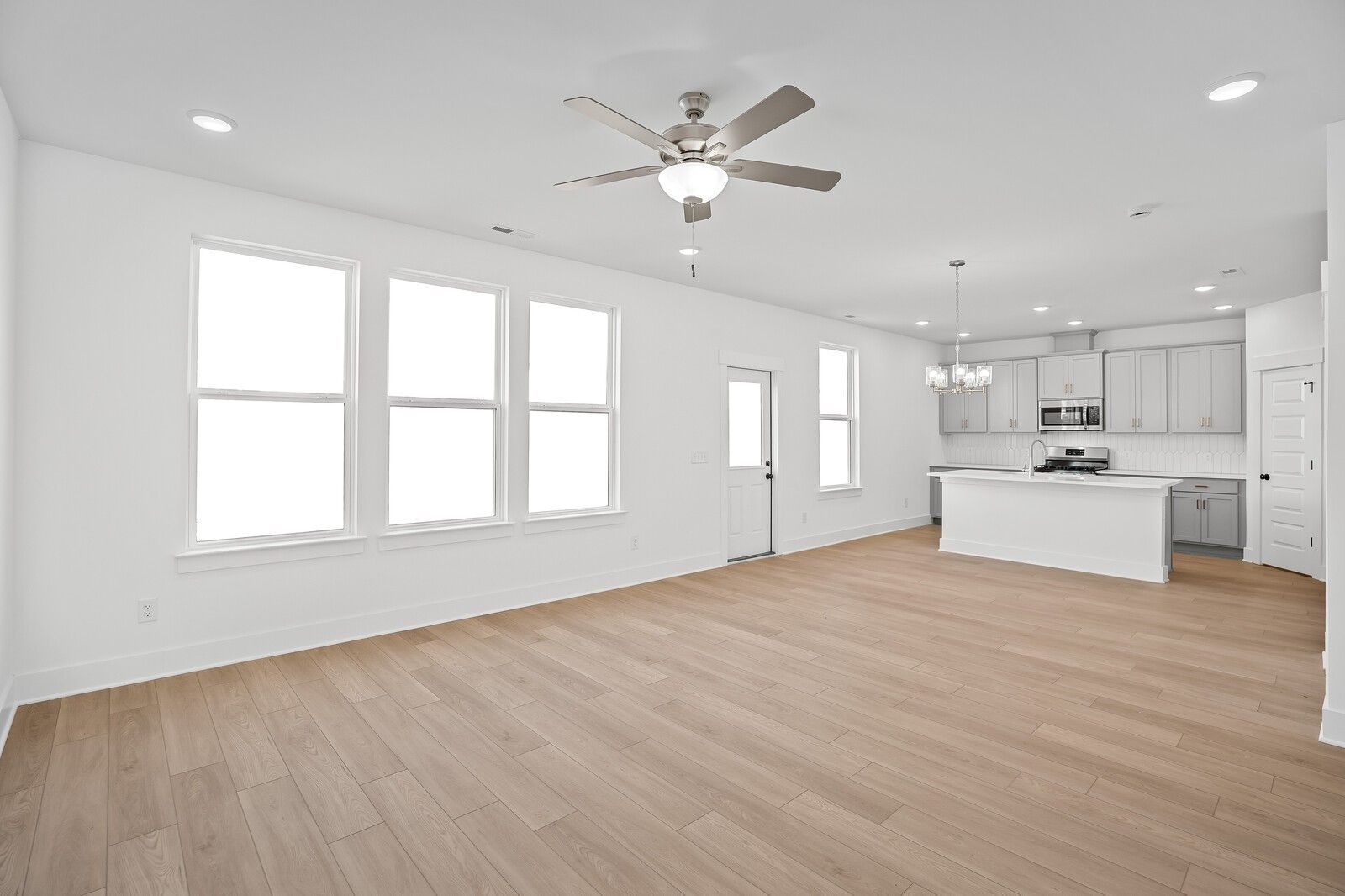 Modern open-concept kitchen with white island, stainless appliances, hardwood floors, and large windows in The Logan C, Gallatin, TN