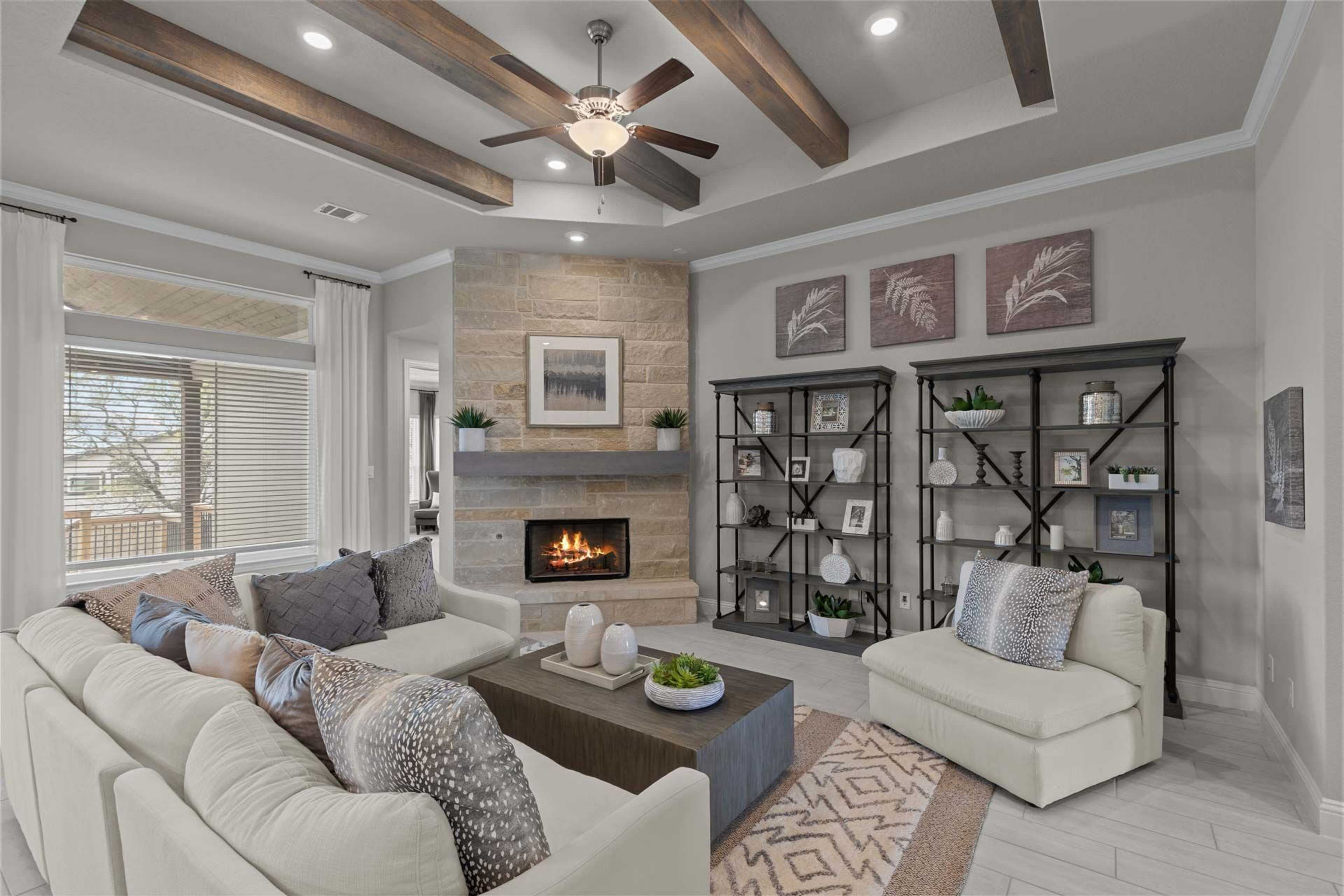 Cozy open-concept living room in Ladera San Antonio TX home with stone fireplace, exposed wood beams, ceiling fan, plush beige sofa and neutral decor
