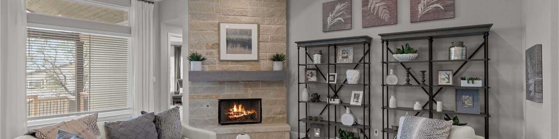 Cozy open-concept living room in Ladera San Antonio TX home with stone fireplace, exposed wood beams, ceiling fan, plush beige sofa and neutral decor