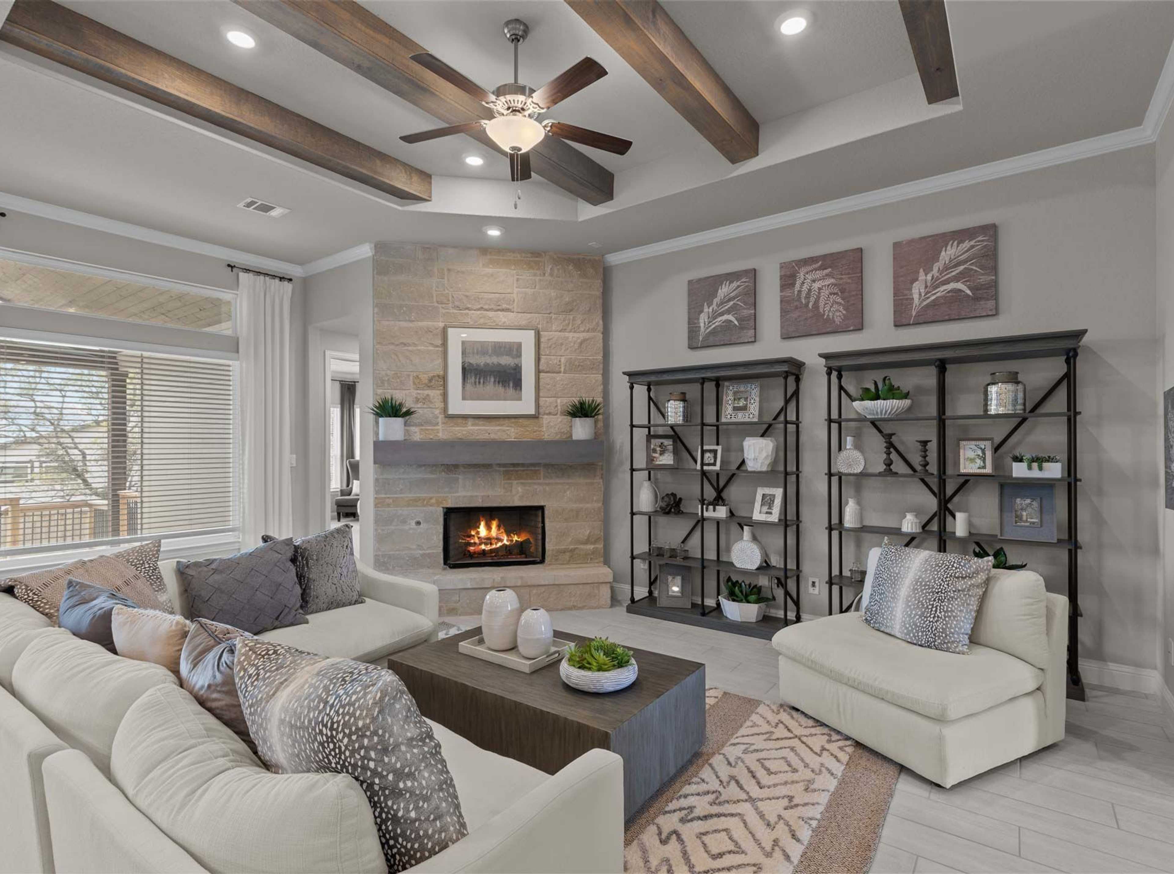 Cozy open-concept living room in Ladera San Antonio TX home with stone fireplace, exposed wood beams, ceiling fan, plush beige sofa and neutral decor