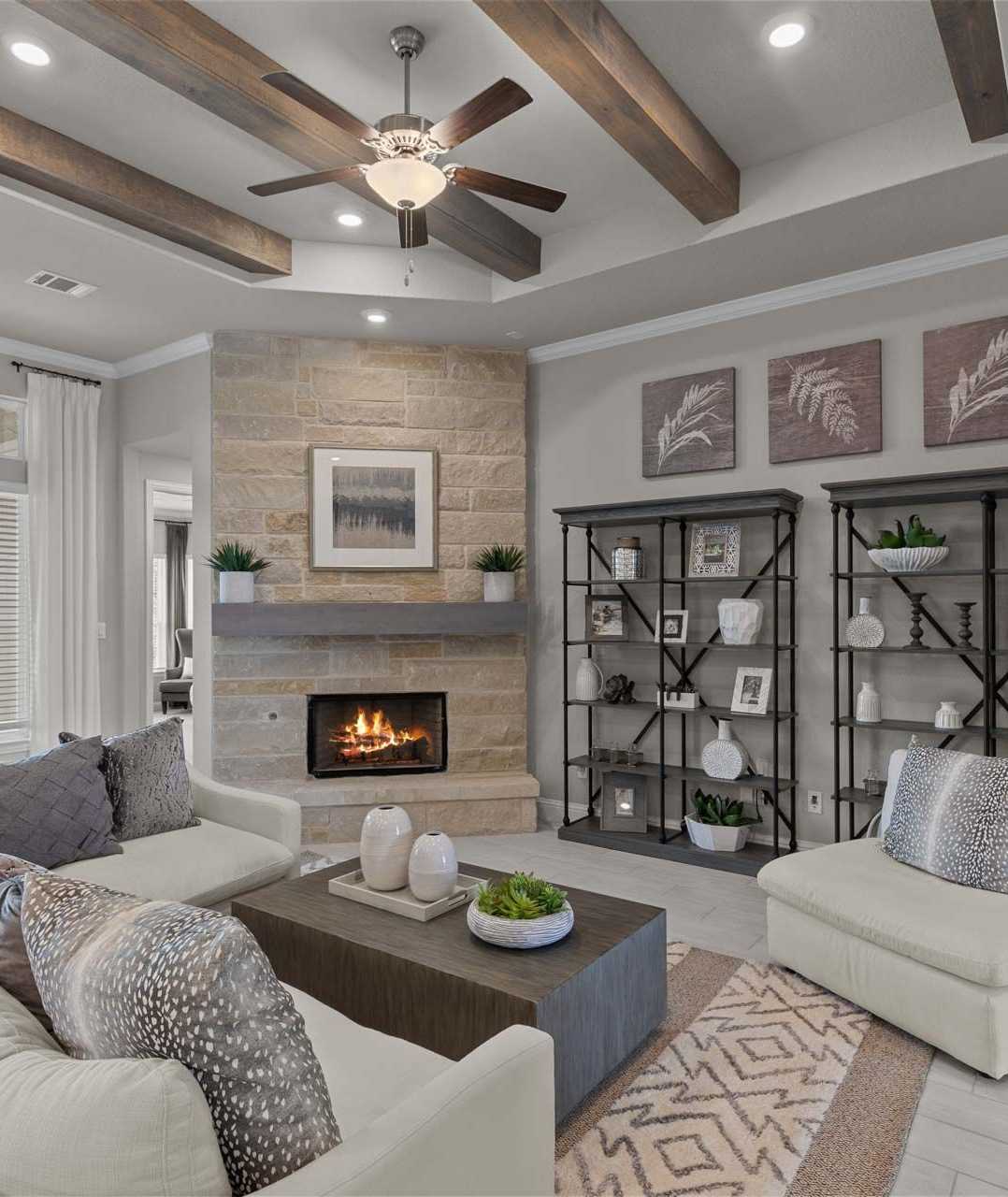 Cozy open-concept living room in Ladera San Antonio TX home with stone fireplace, exposed wood beams, ceiling fan, plush beige sofa and neutral decor