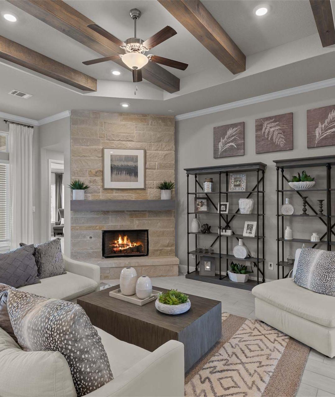 Cozy open-concept living room in Ladera San Antonio TX home with stone fireplace, exposed wood beams, ceiling fan, plush beige sofa and neutral decor