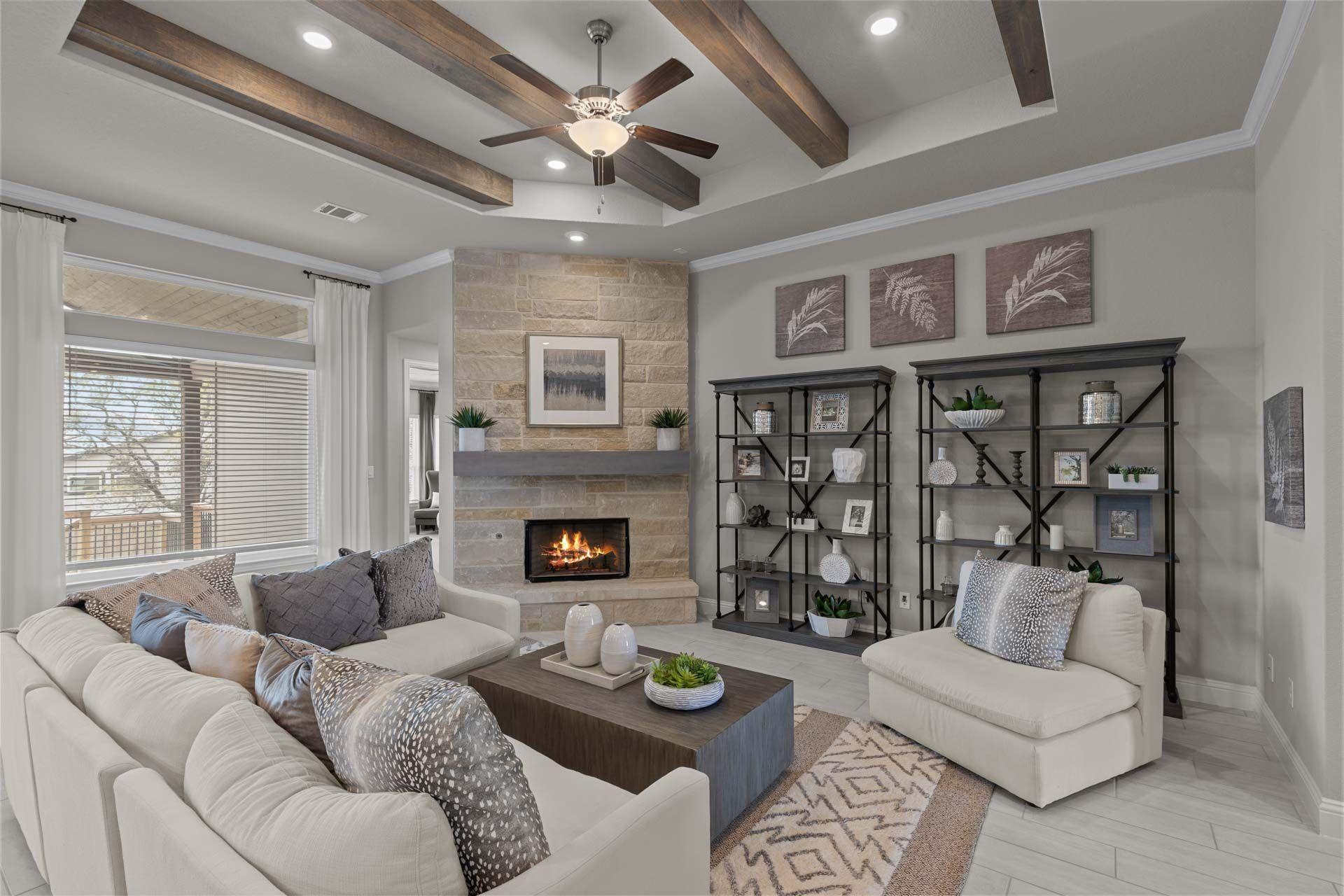 Cozy open-concept living room in Ladera San Antonio TX home with stone fireplace, exposed wood beams, ceiling fan, plush beige sofa and neutral decor