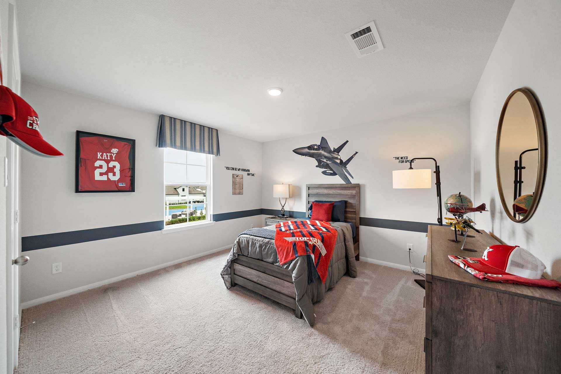 Teen boy's bedroom at Sunterra in Katy Texas with aviation posters, red sports decor, gray bed, and wooden dresser