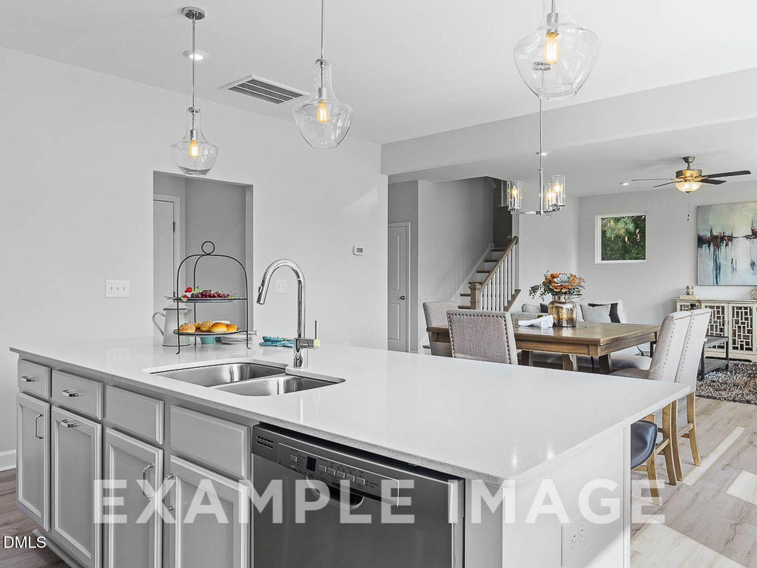 Modern open-concept kitchen with white island, stainless dishwasher, pendant lights, and adjacent dining in The Chestnut B, Lillington, NC