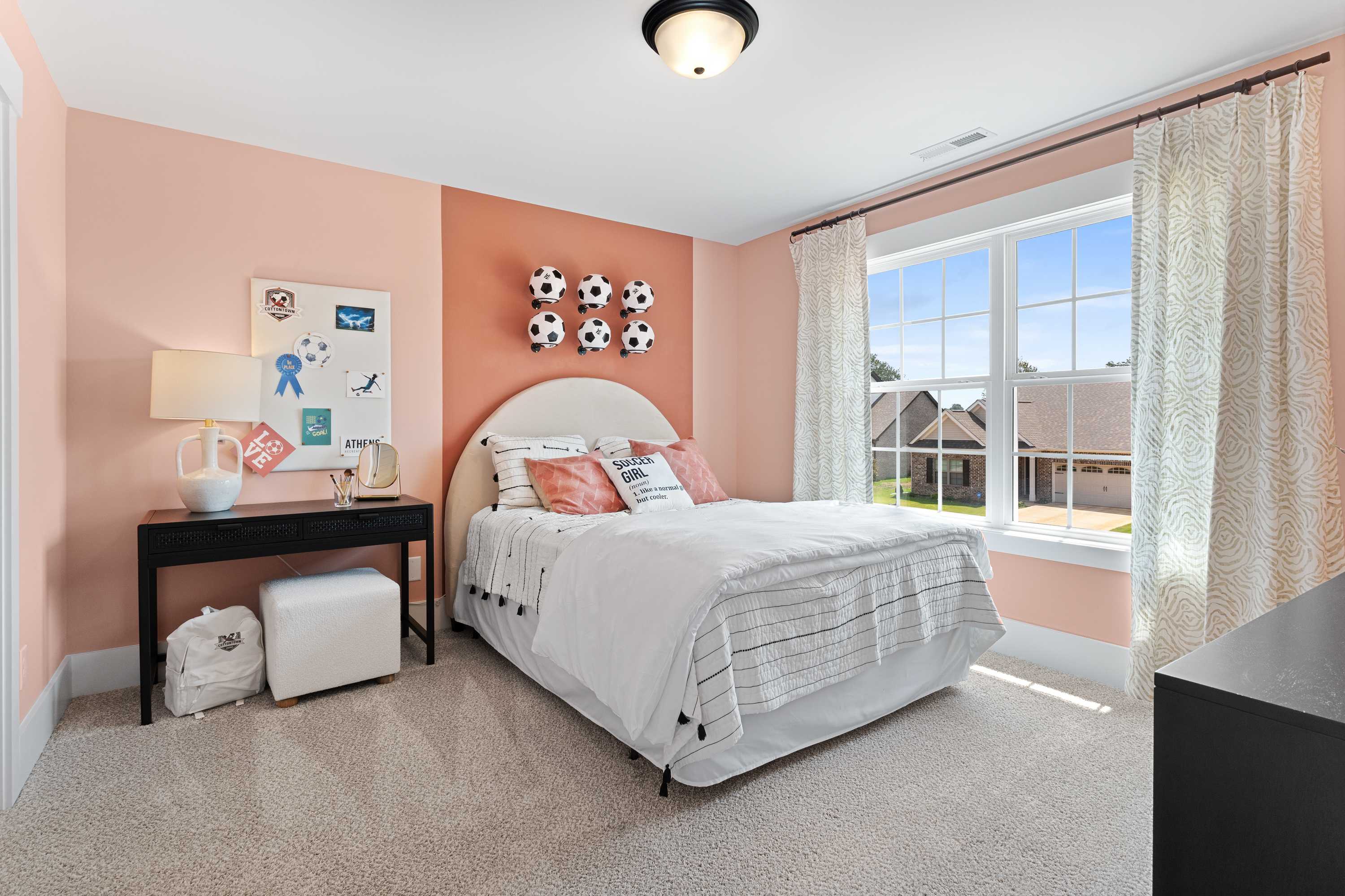 Cozy pink bedroom in The Shelby A showcasing tufted bed, soccer ball wall decor, and neighborhood window view