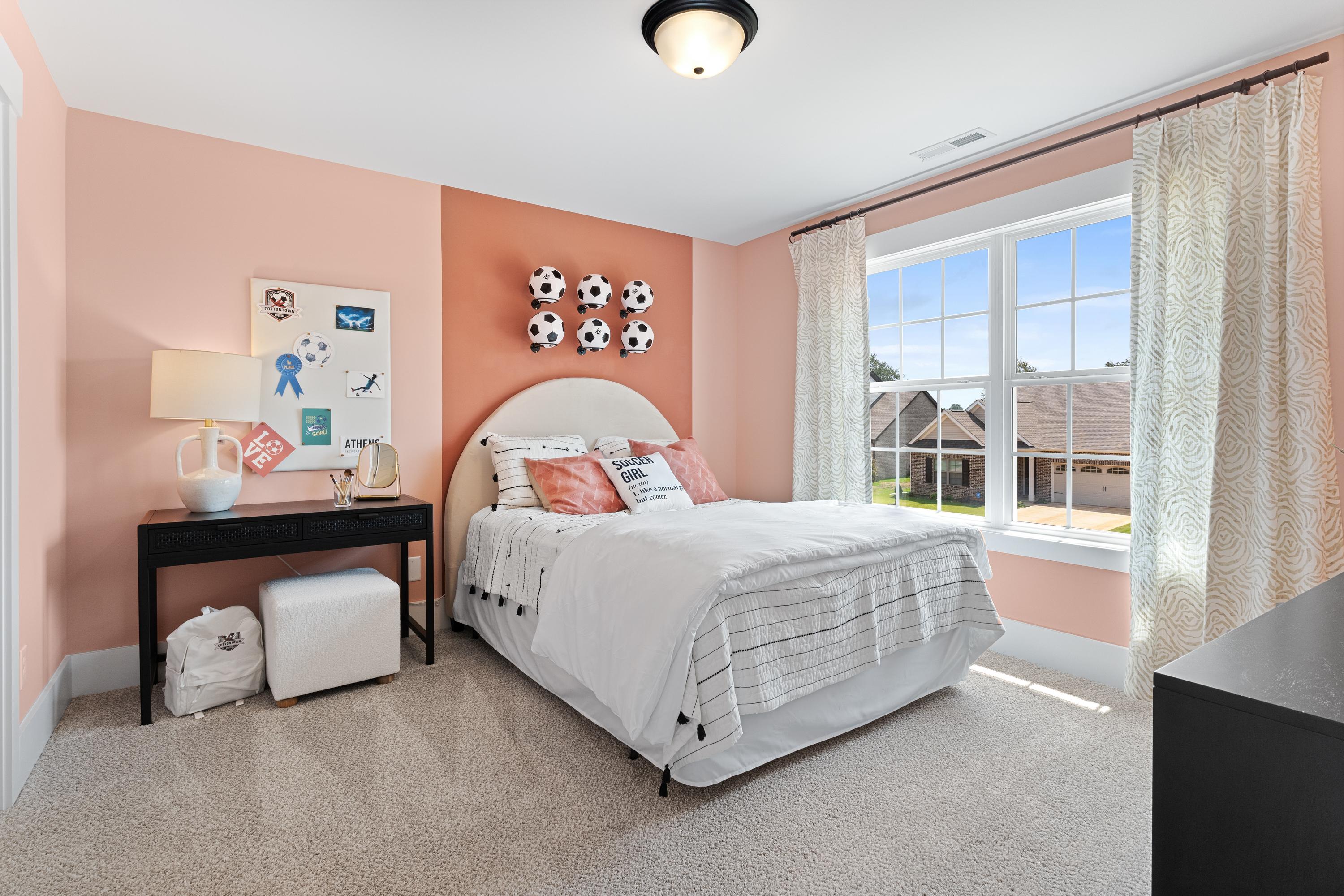 Cozy pink bedroom in The Shelby A showcasing tufted bed, soccer ball wall decor, and neighborhood window view