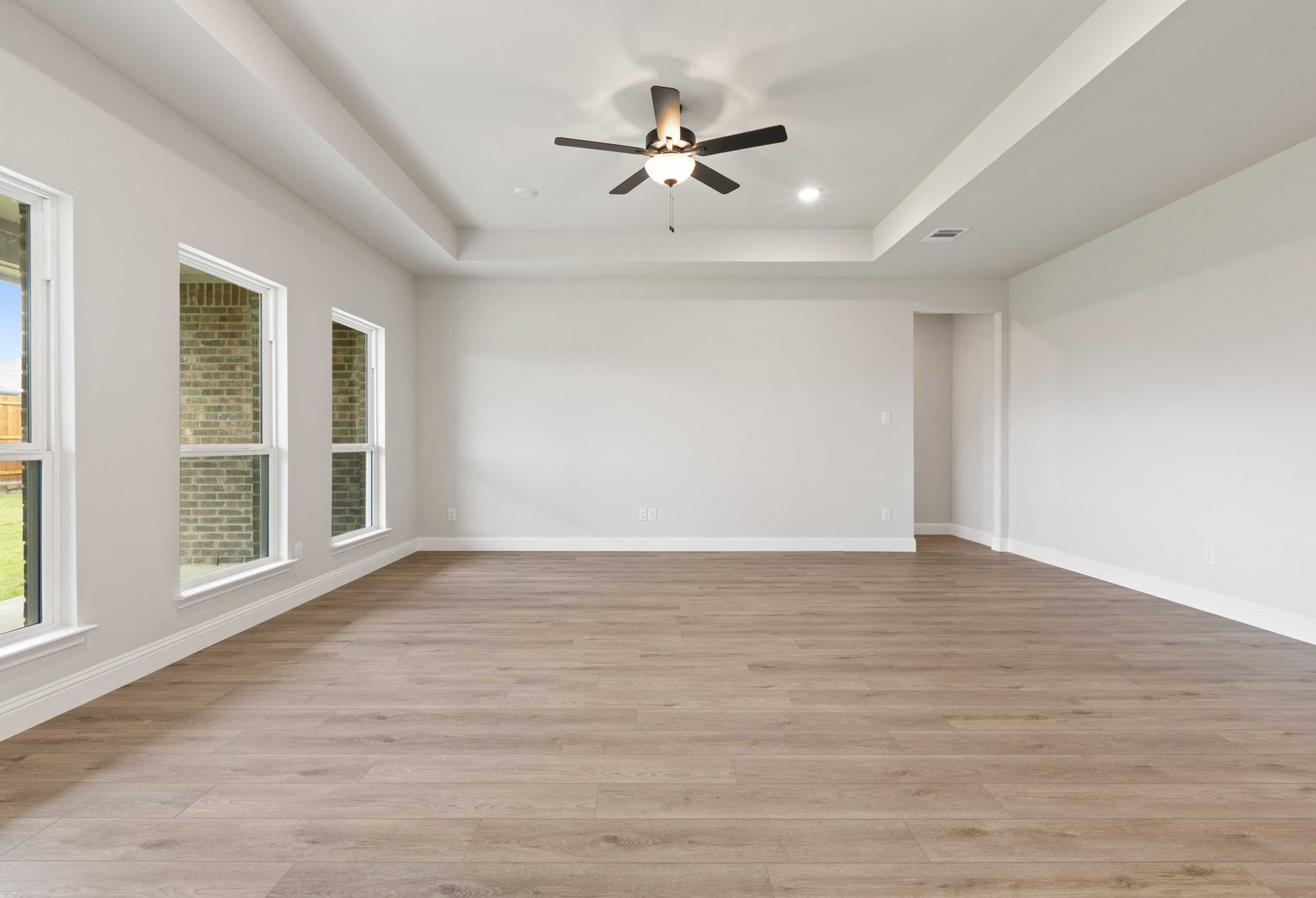 Spacious living room in The Harrison C home design by Davidson Homes with hardwood floors, large windows, and ceiling fan