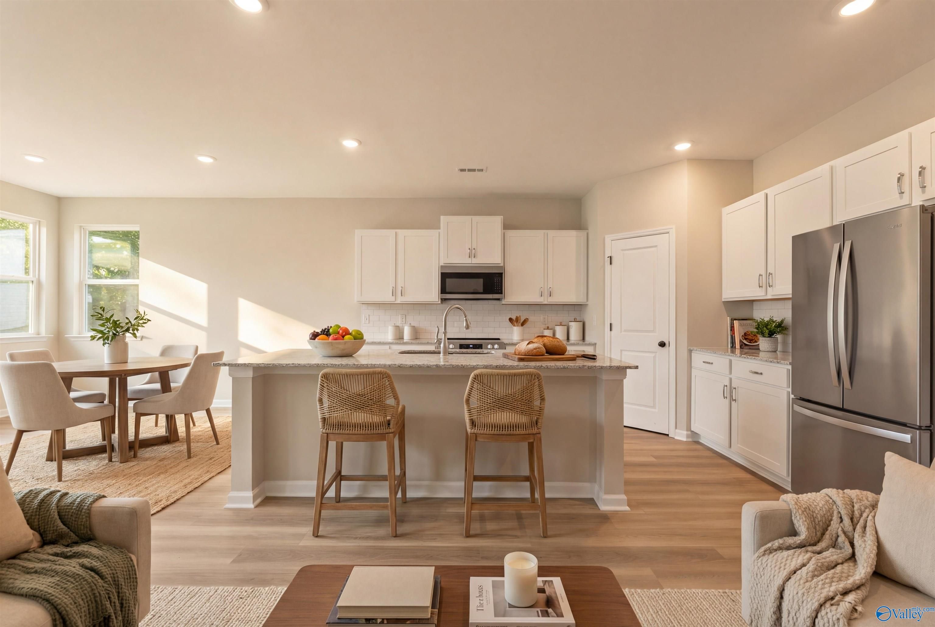 Open-concept kitchen and living room with white shaker cabinets, stainless steel appliances, and island bar in Davidson Homes The Phoenix, Fayetteville, TN