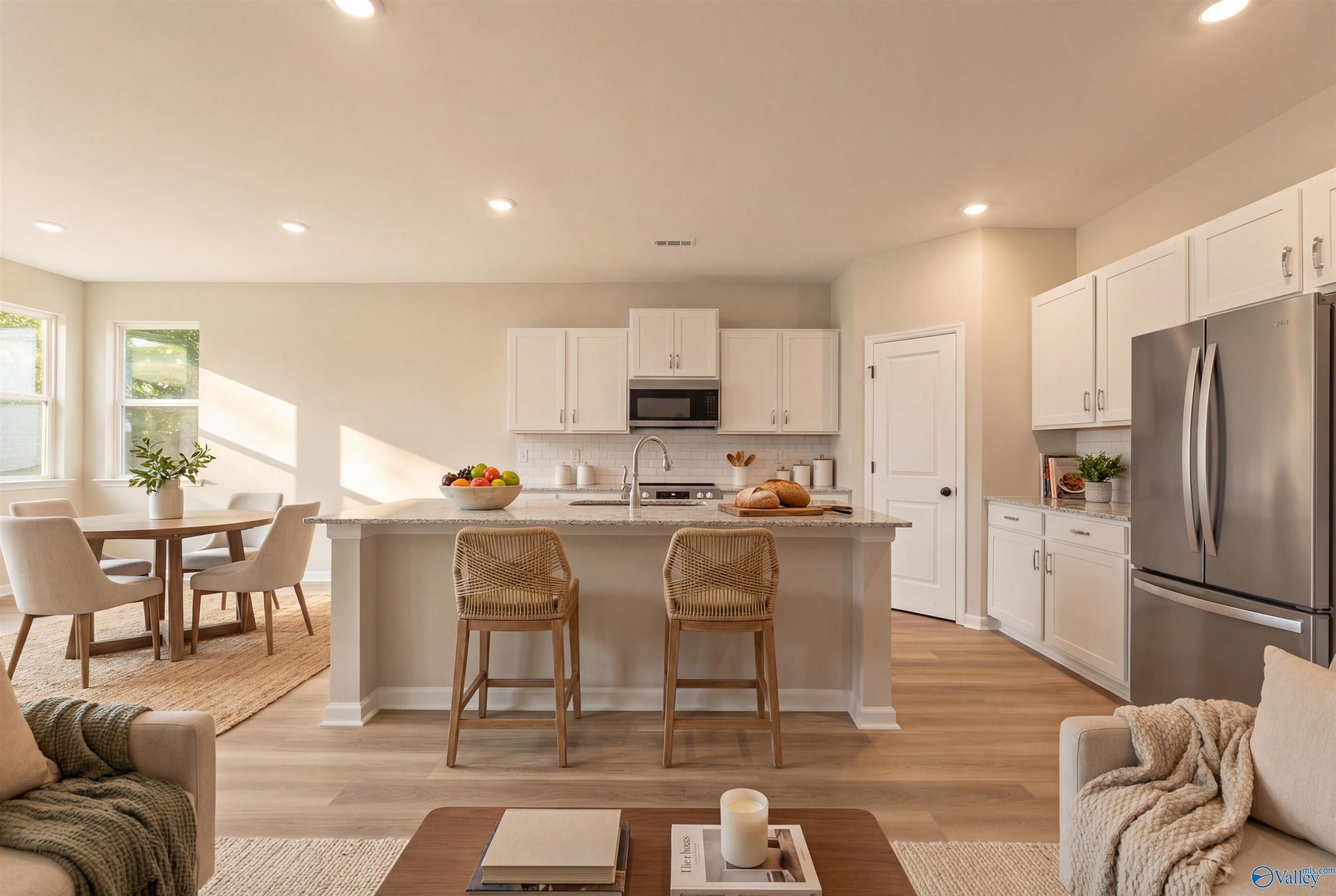 Open-concept kitchen and living room with white shaker cabinets, stainless steel appliances, and island bar in Davidson Homes The Phoenix, Fayetteville, TN