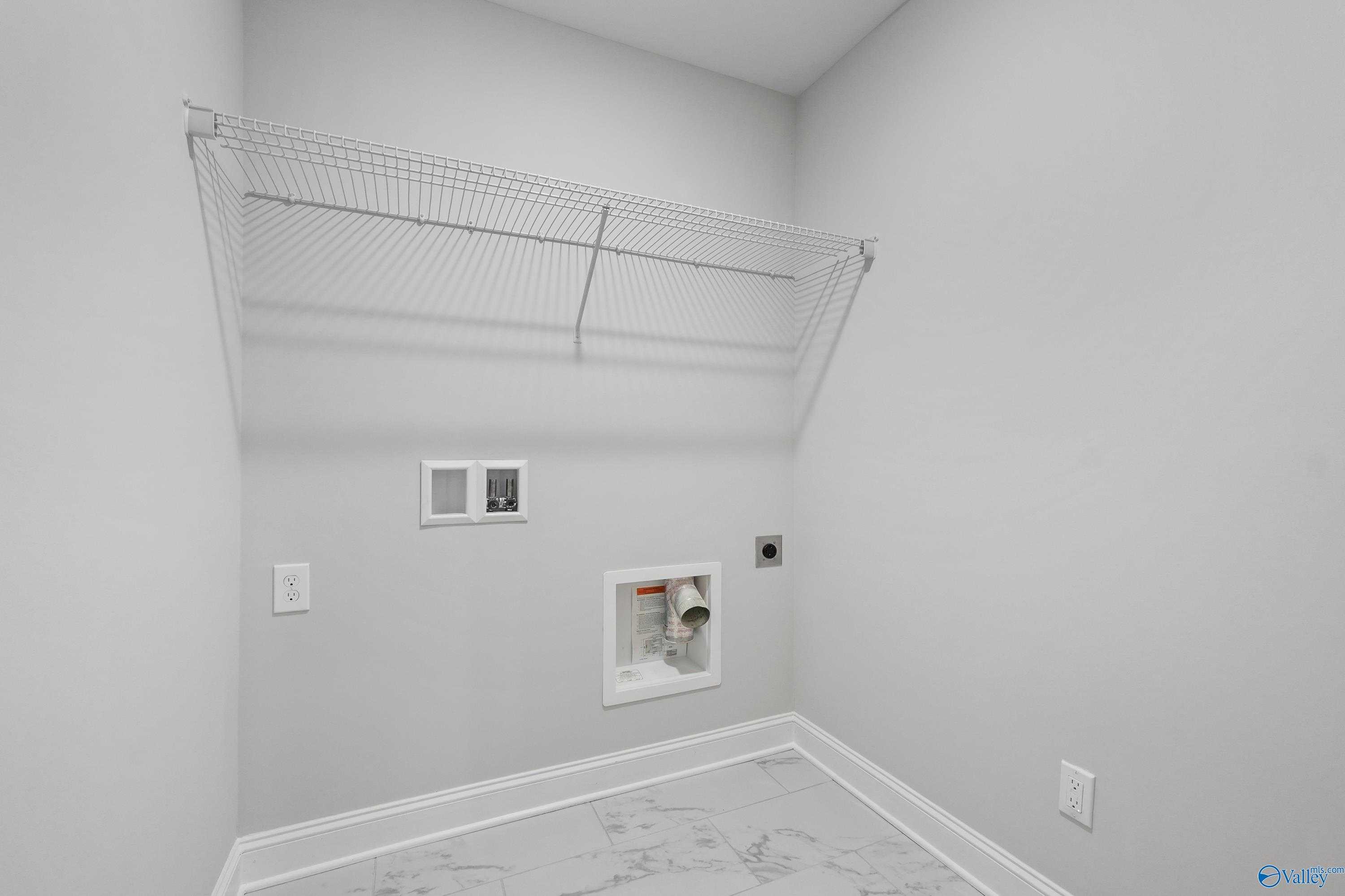 Modern laundry room featuring wire shelving, washer-dryer hookups, and marble flooring in Davidson Homes The Camden B, Huntsville, AL