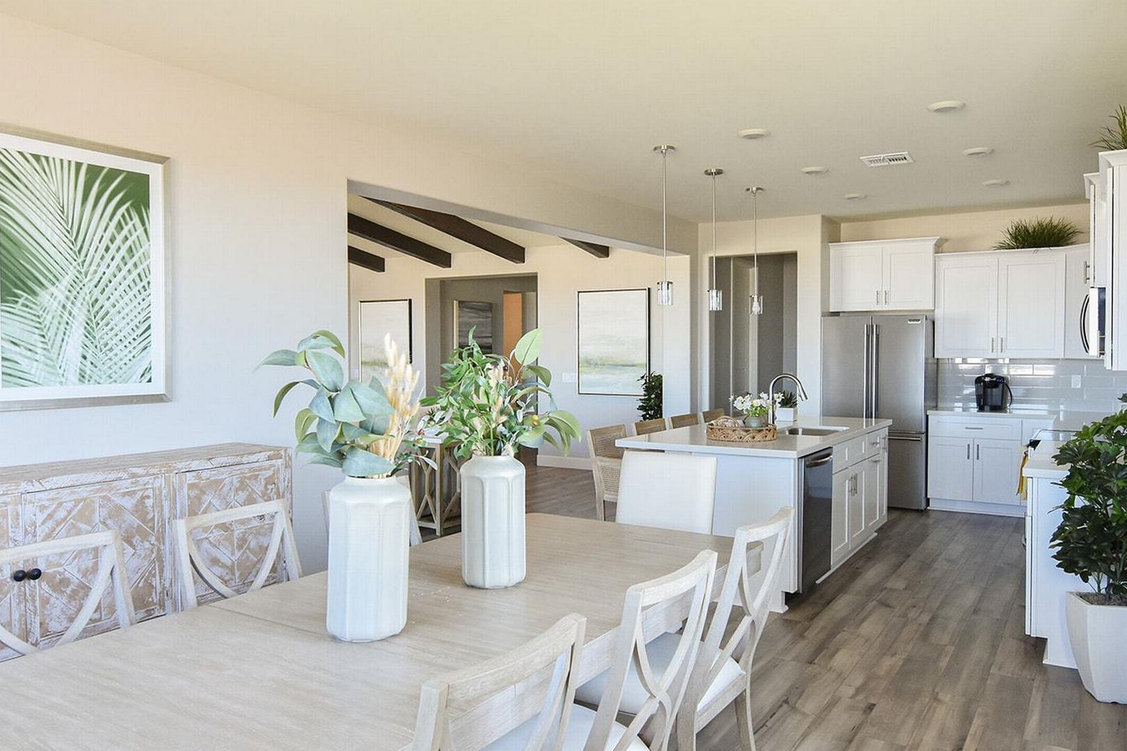 Open-concept dining and kitchen in The Summit E featuring long wooden table, white island, stainless appliances, and lush plant accents