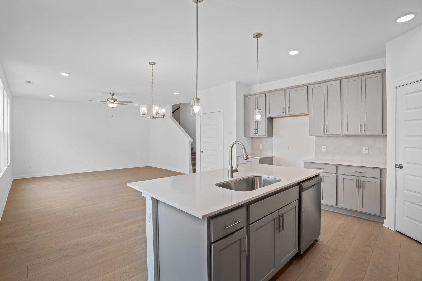 Modern open-concept kitchen with white shaker cabinets, large island sink, pendant lights, and hardwood floors in The Logan B, Calista Farms