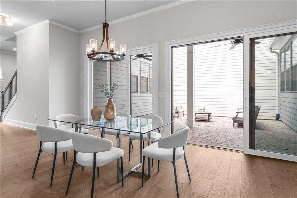 Elegant dining room with glass table, white chairs, and chandelier opening to covered patio in The Seaside B home, Woodstock, Georgia