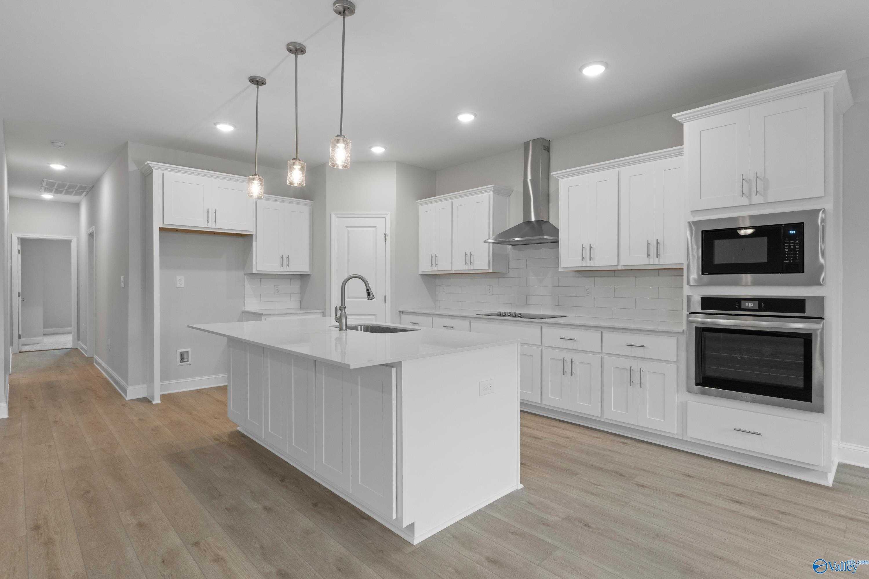 Modern white kitchen with quartz island, stainless double ovens, pendant lights in Davidson Homes The Rockford B, Toney, Alabama