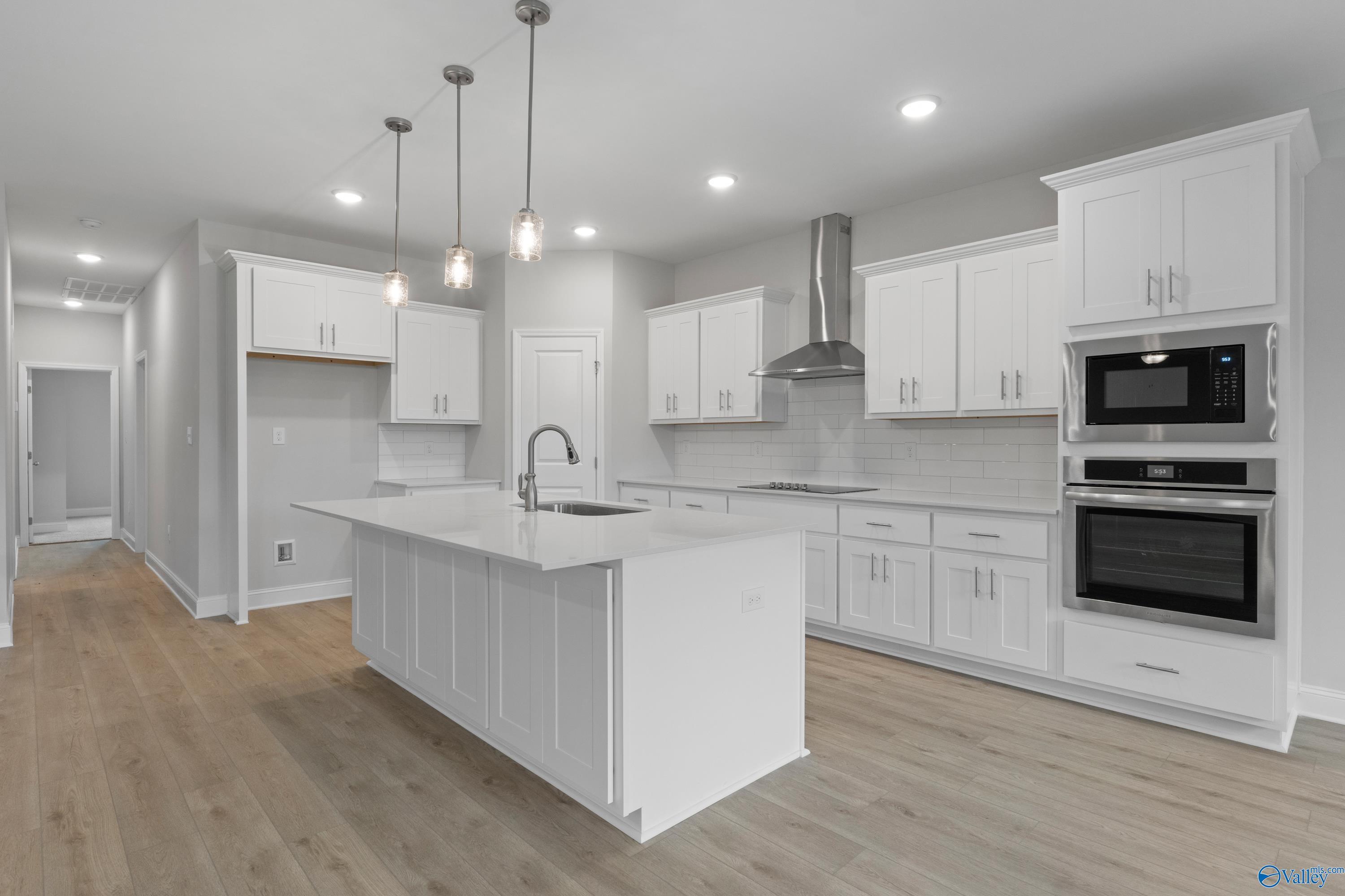 Modern white shaker kitchen with quartz island sink, stainless double oven, and pendant lights in Davidson Homes The Rockford B, Toney, Alabama