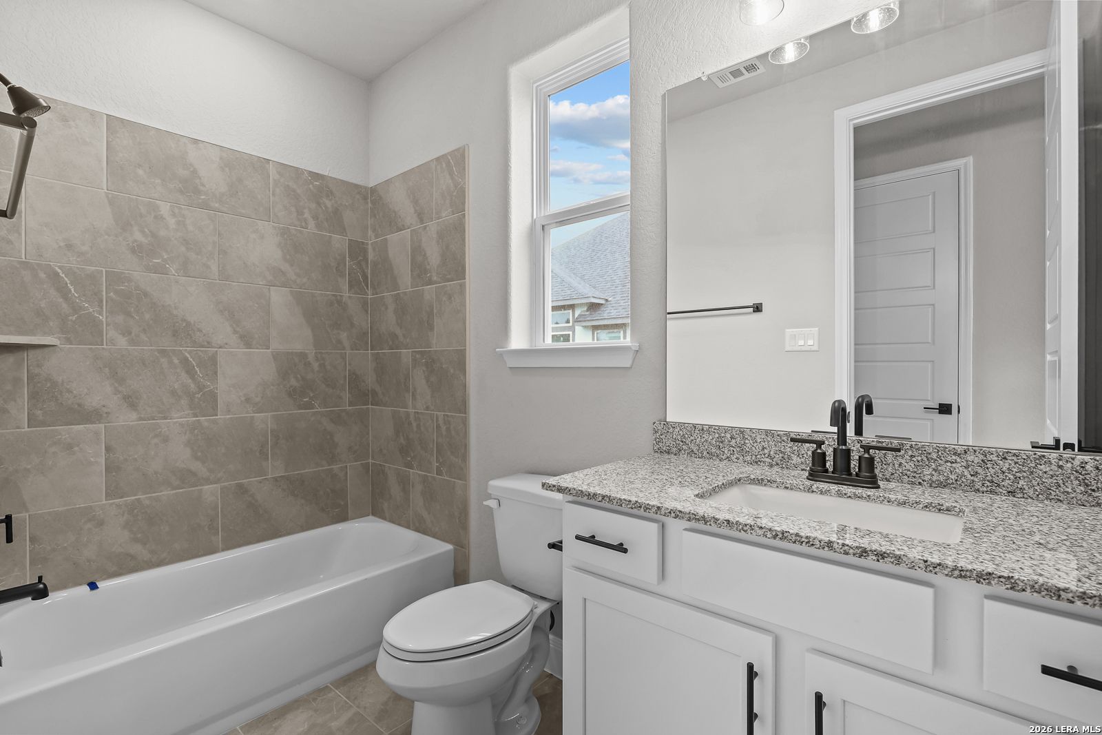 Modern guest bathroom featuring granite vanity, soaking tub, marble-look tiles in The Belmont H, Castroville, Texas