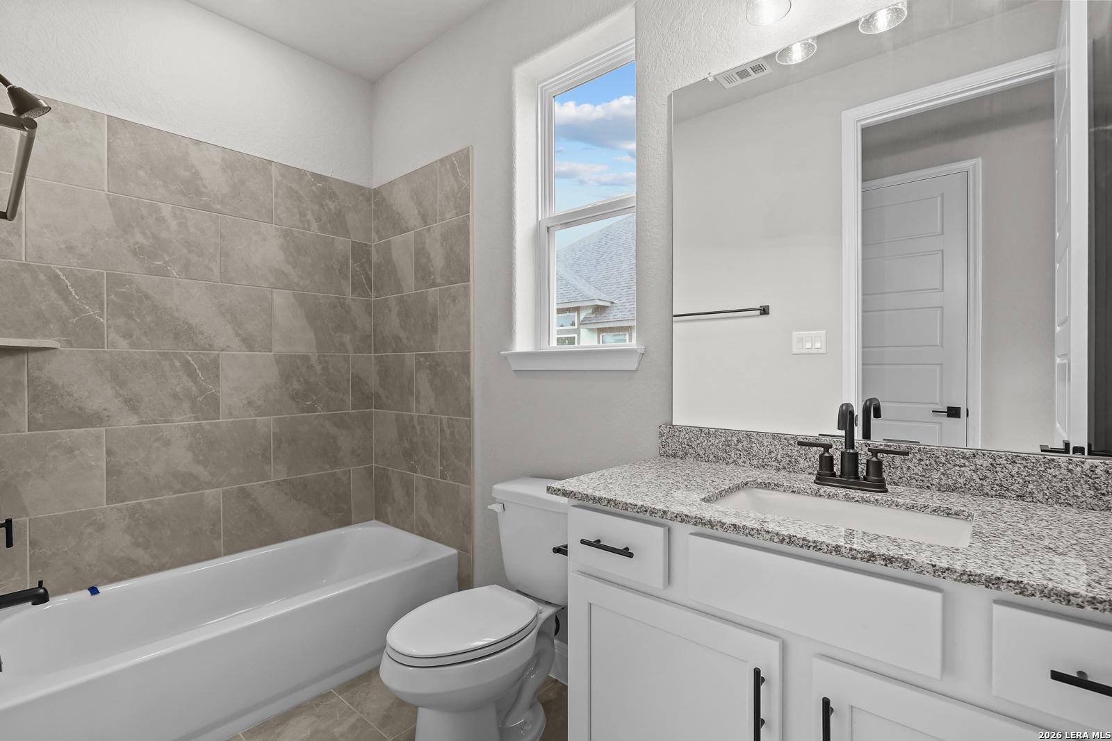 Modern guest bathroom featuring granite vanity, soaking tub, marble-look tiles in The Belmont H, Castroville, Texas